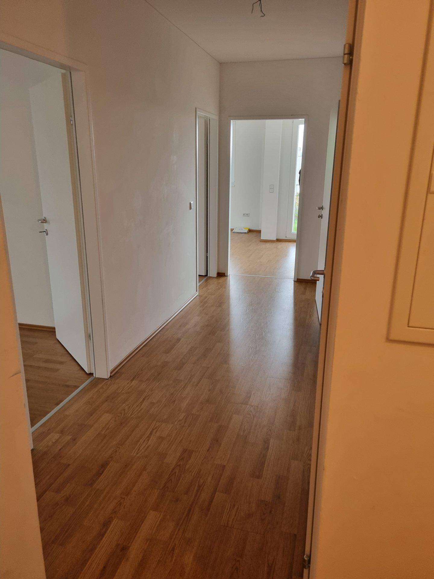 Heller Flur mit Laminatboden und weißen Wänden, der zu verschiedenen Zimmern führt.