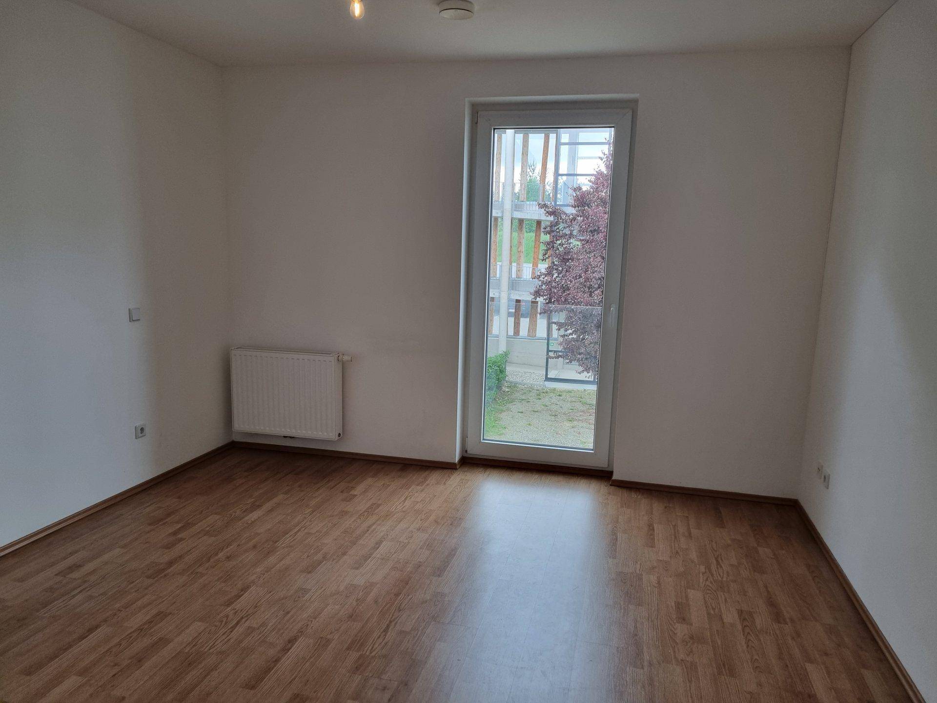 Leeres Schlafzimmer mit Laminatboden, weiß gestrichenen Wänden und einem großen Fenster.