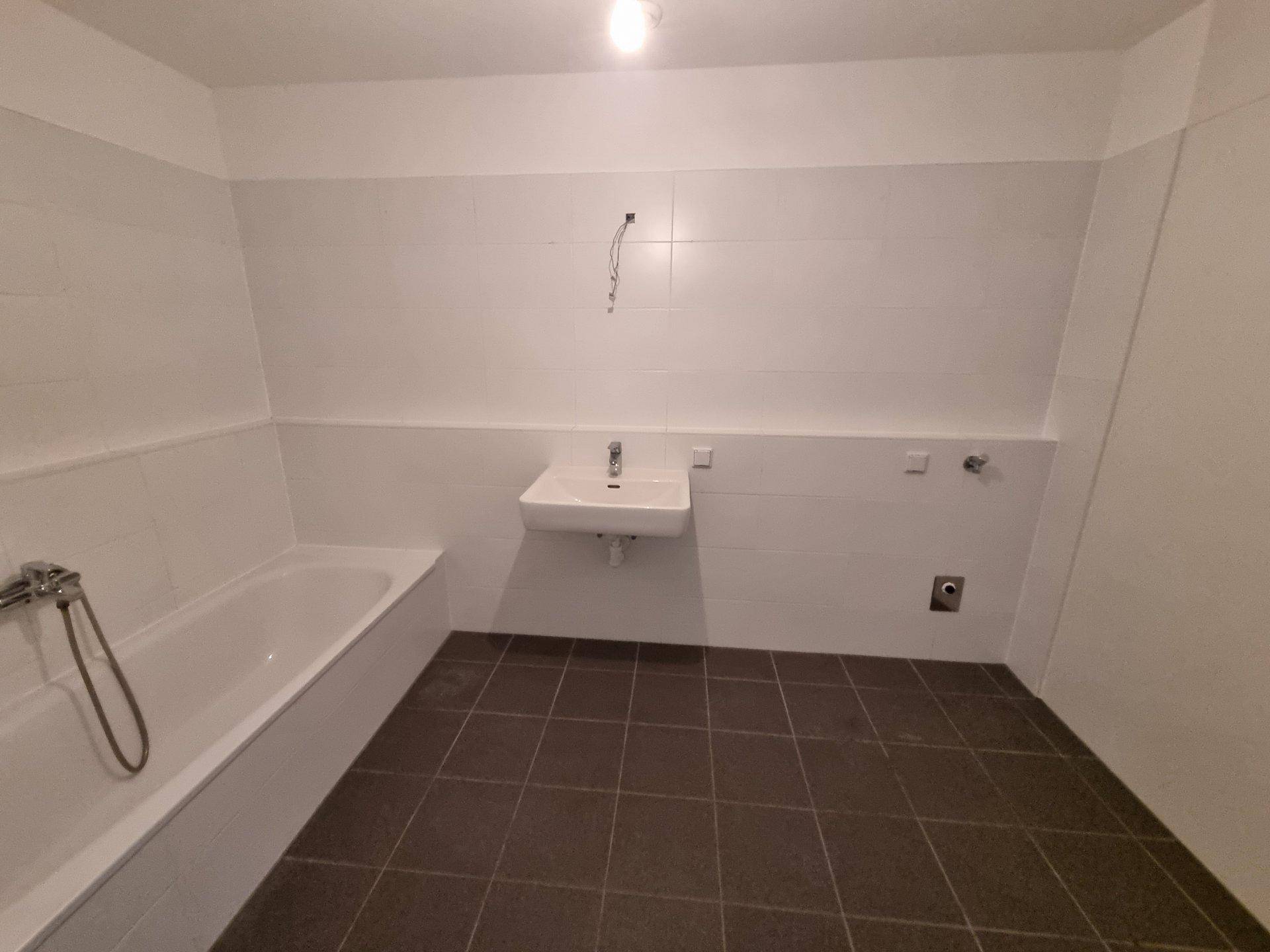 Helles Badezimmer mit Badewanne, Waschbecken und weißen Fliesen, bereit zur Fertigstellung.