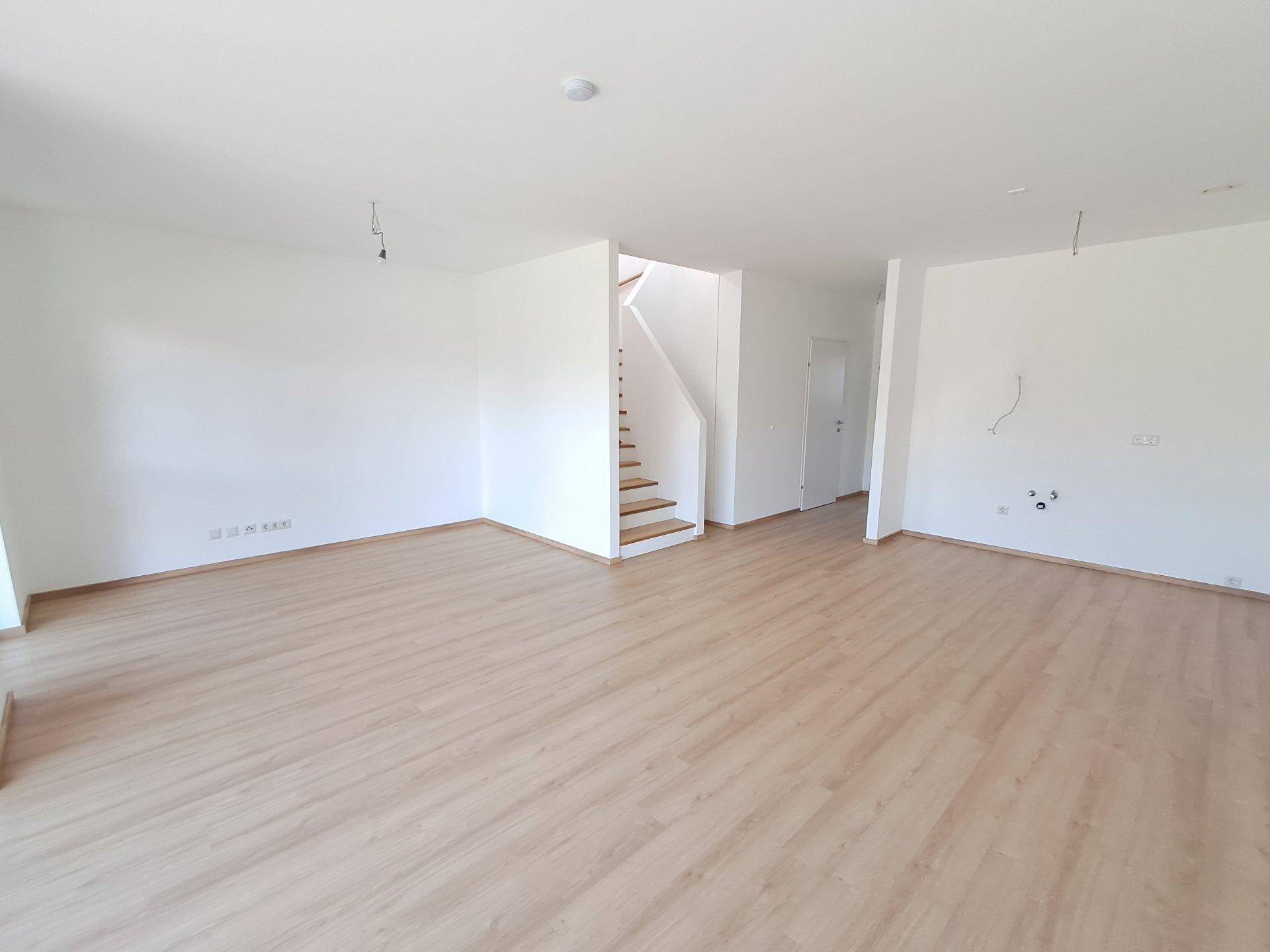 Geräumiger, leerer Wohnbereich mit Holztreppe und hellem Laminatboden, bereit zur Einrichtung.