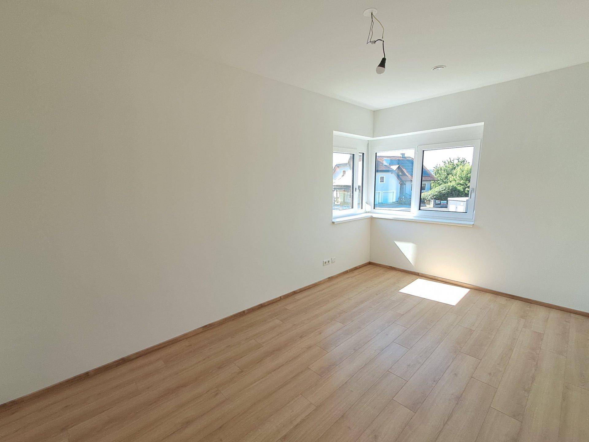 Leeres Schlafzimmer mit Eckfenstern und hellem Laminatboden, bietet viel natürliches Licht.