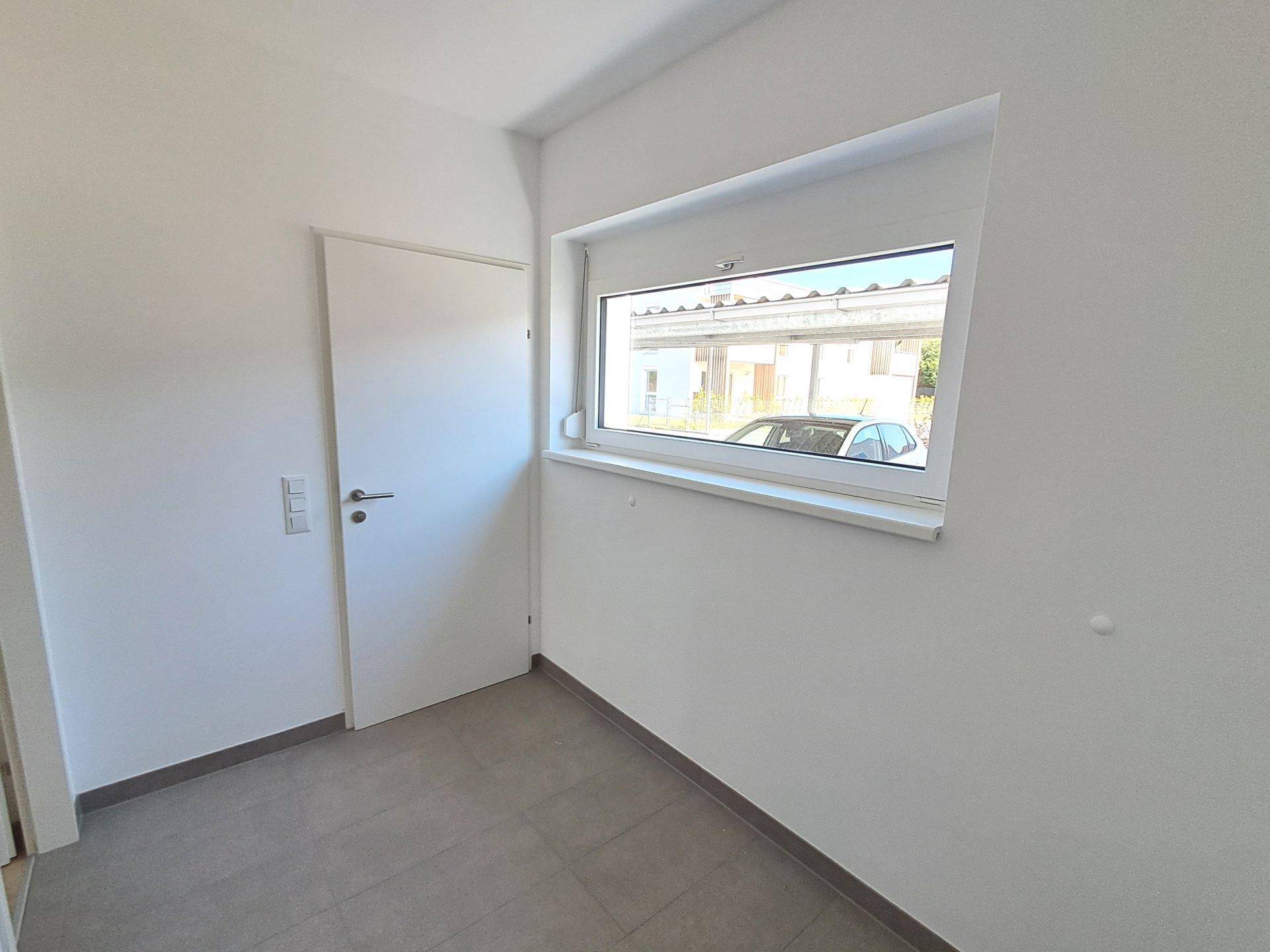 Leerer Raum mit Fenster und Tür, bereit für individuelle Gestaltung, mit Fliesenboden.