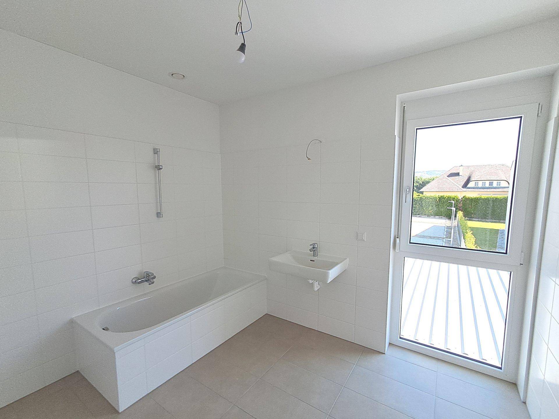 Leeres Badezimmer mit Badewanne, Waschbecken und Zugang zu einem Balkon oder einer Terrasse.