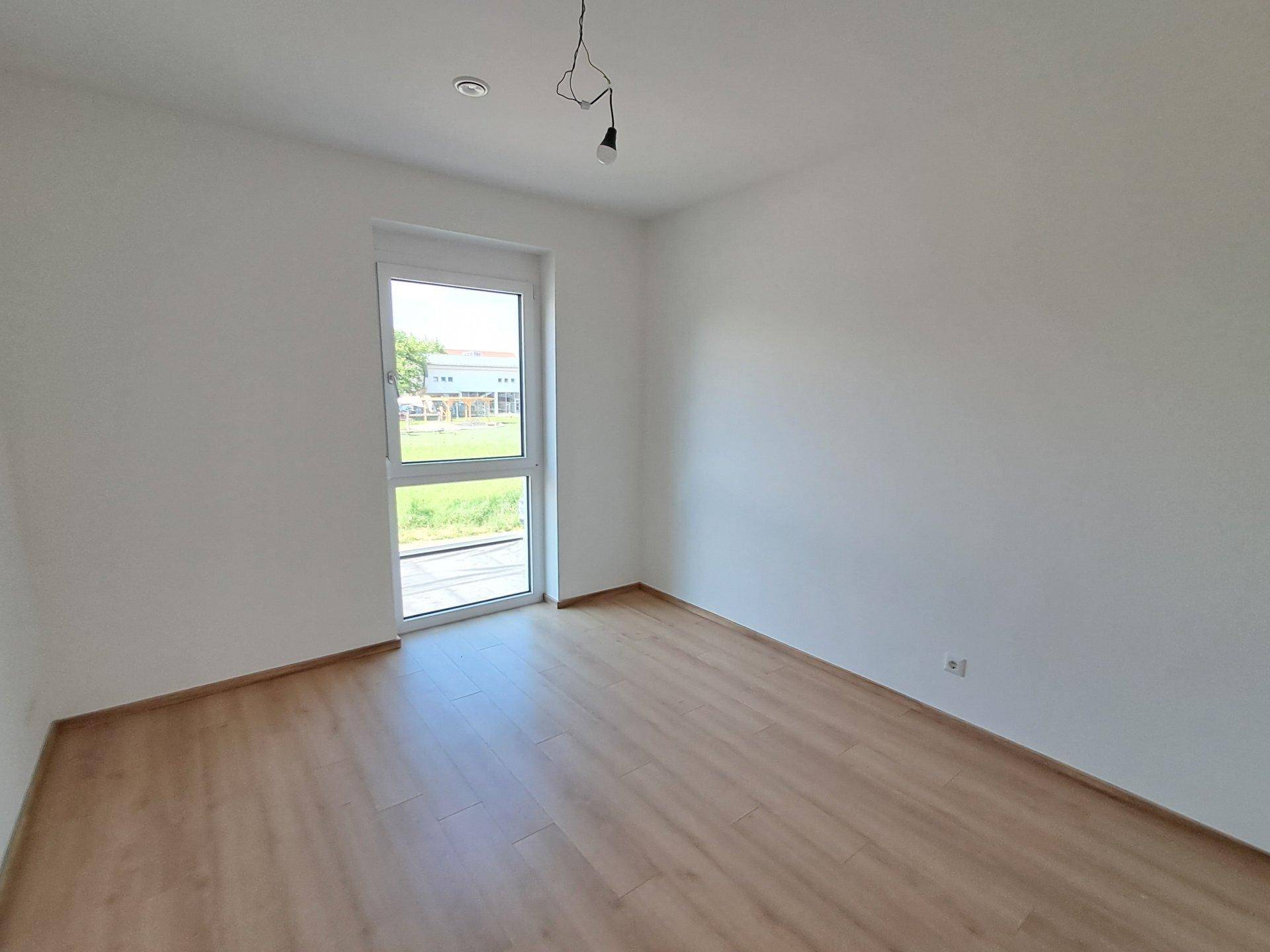 Leeres Schlafzimmer mit Laminatboden und Fenster, bietet viel Tageslicht und Blick ins Grüne.