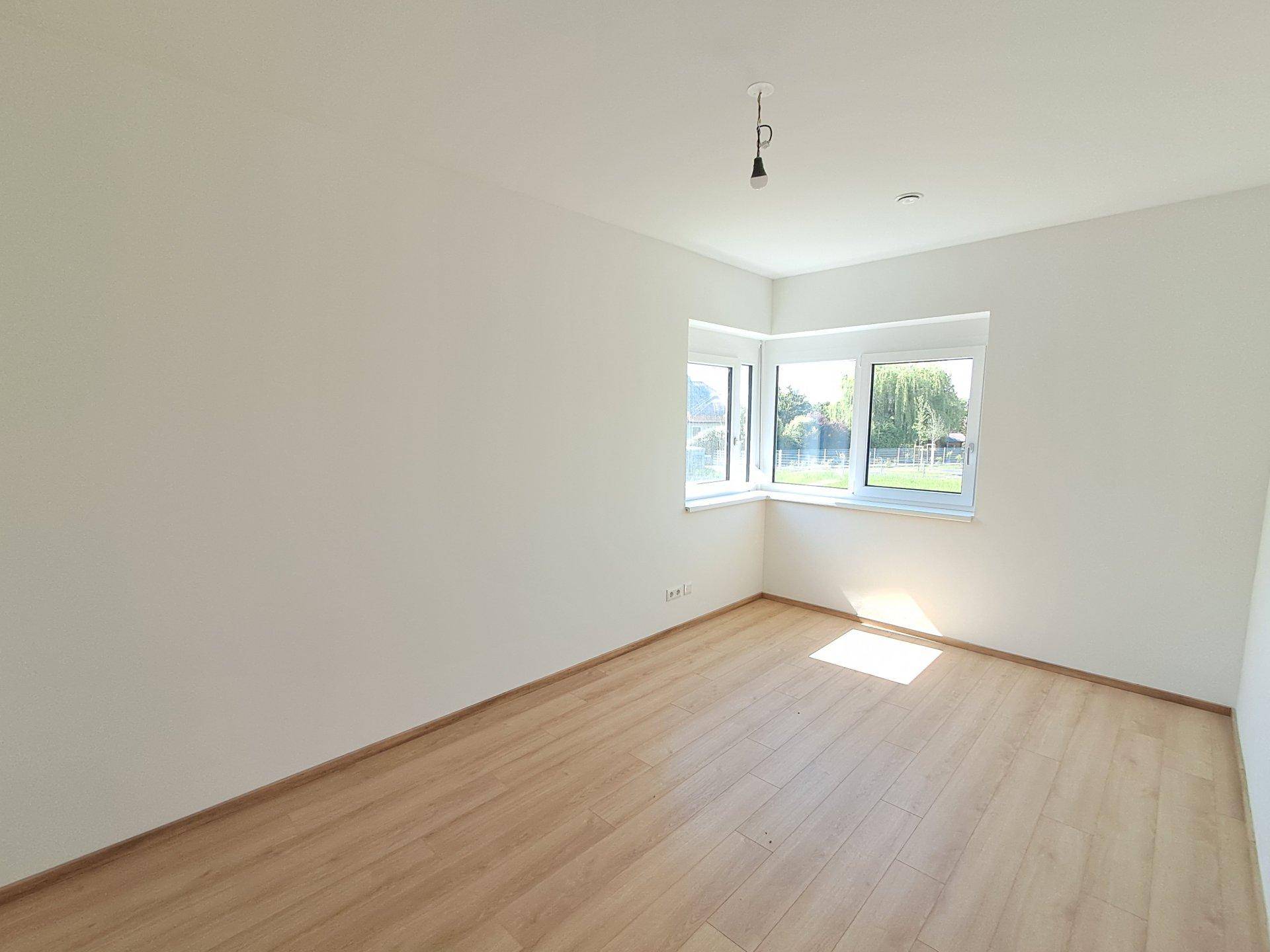 Geräumiges Schlafzimmer mit Eckfenstern und hellem Holzboden, ideal für natürliches Licht.