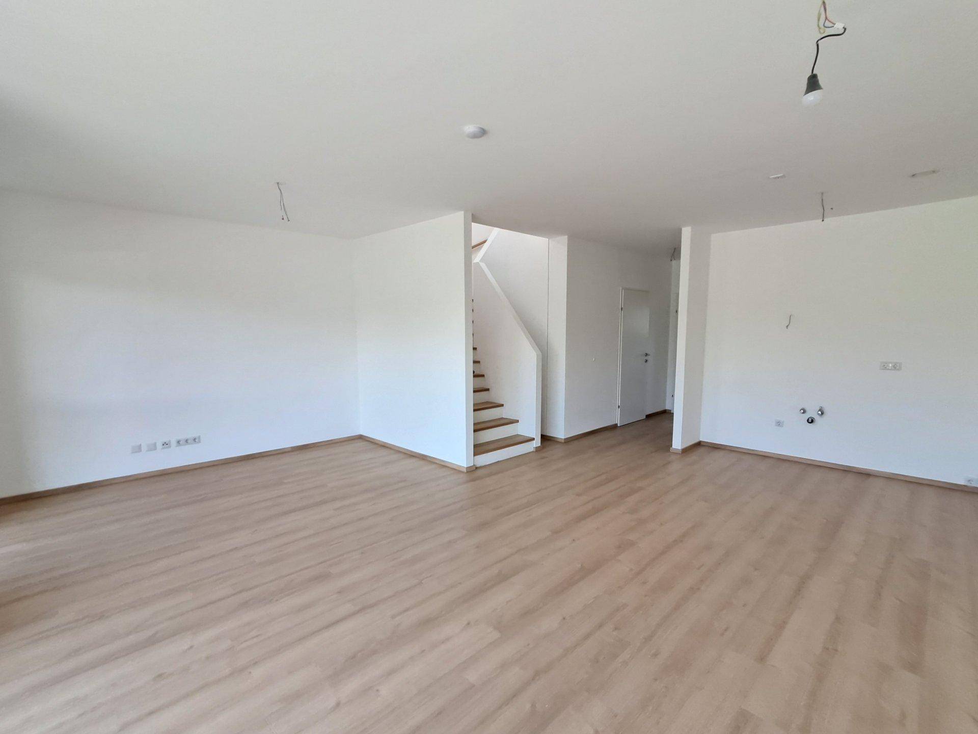 Geräumiger, unmöblierter Wohnbereich mit hellem Holzboden und Treppenaufgang.