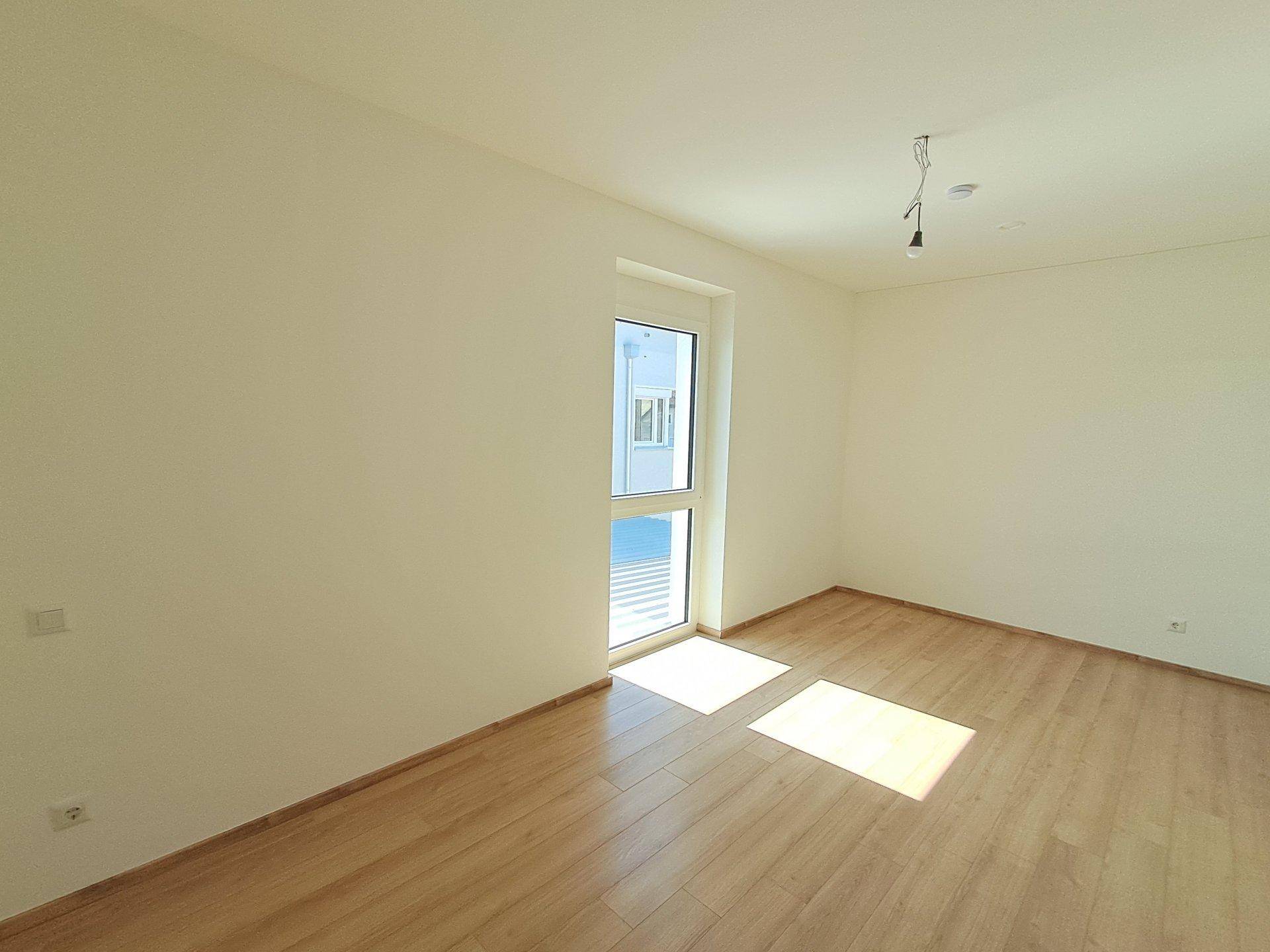 Helles Zimmer mit Holzboden und Zugang nach draußen, ideal als Schlaf- oder Arbeitszimmer.