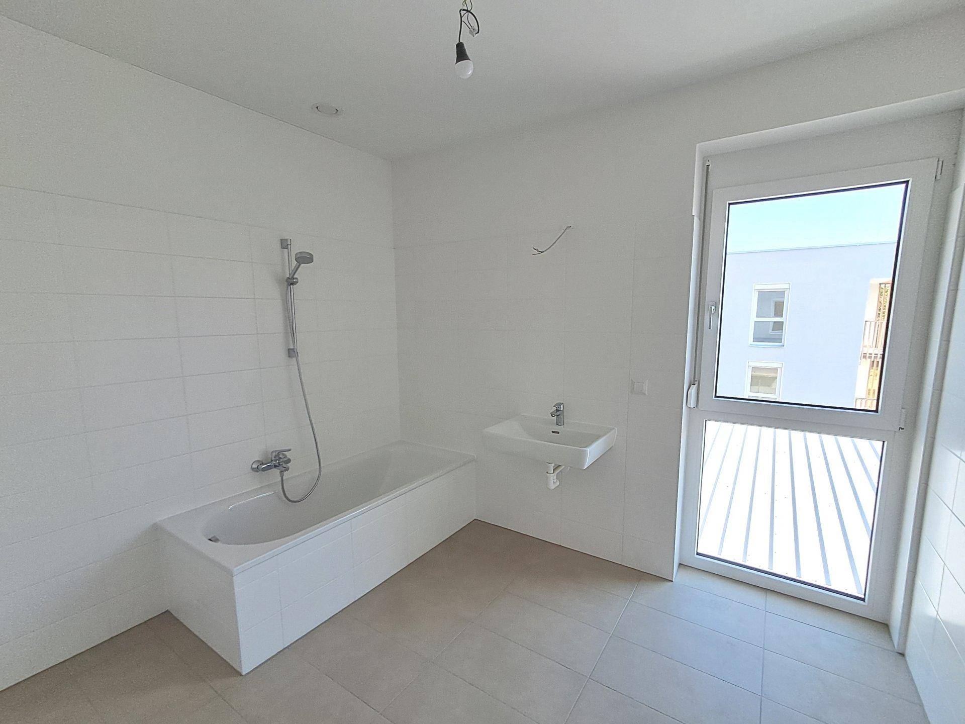 Geräumiges Badezimmer mit Badewanne, Waschbecken und Fenster für natürliche Belüftung.