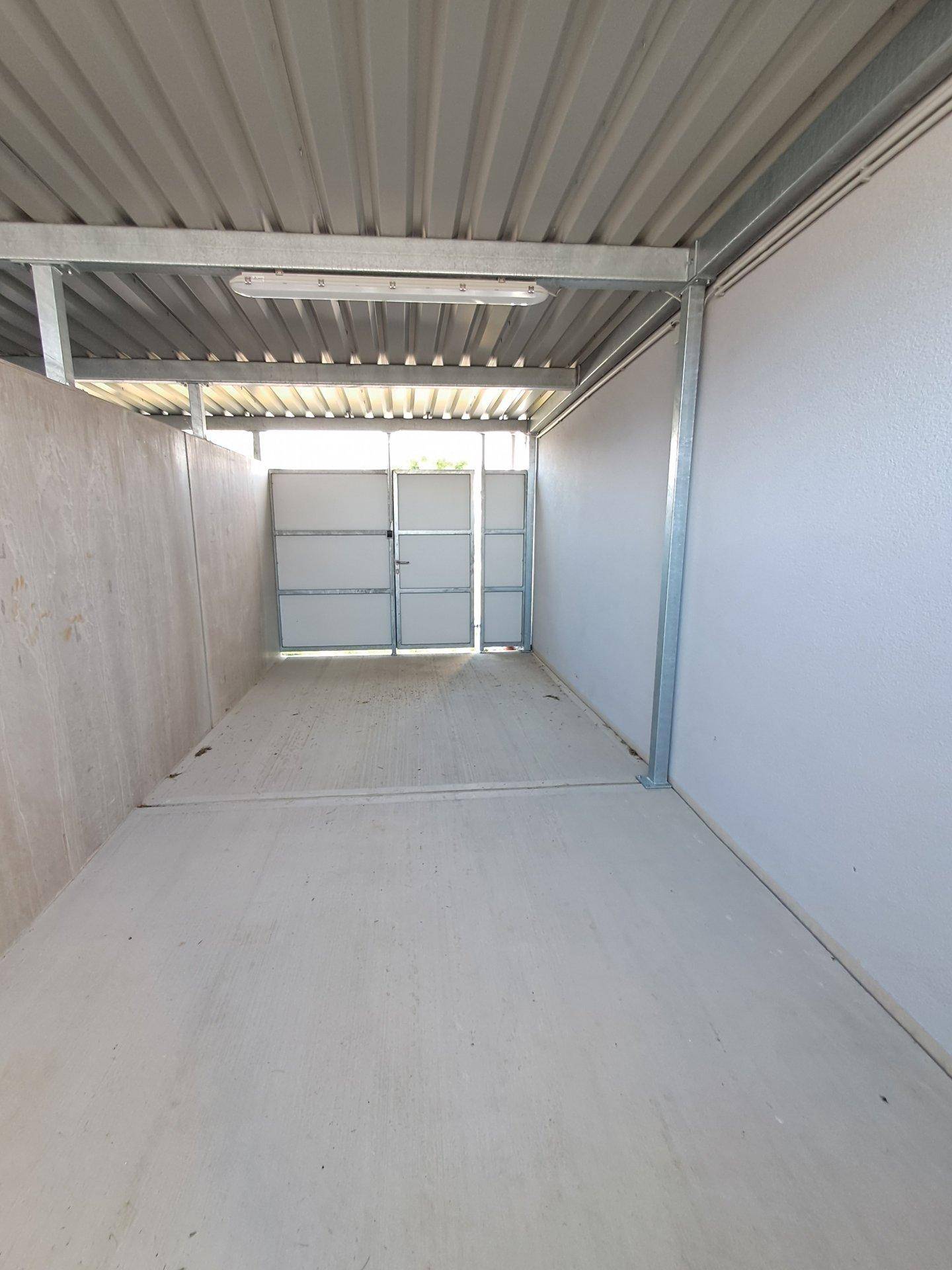 Überdachter Abstellbereich oder Carport mit Betonboden und robuster Metallkonstruktion.