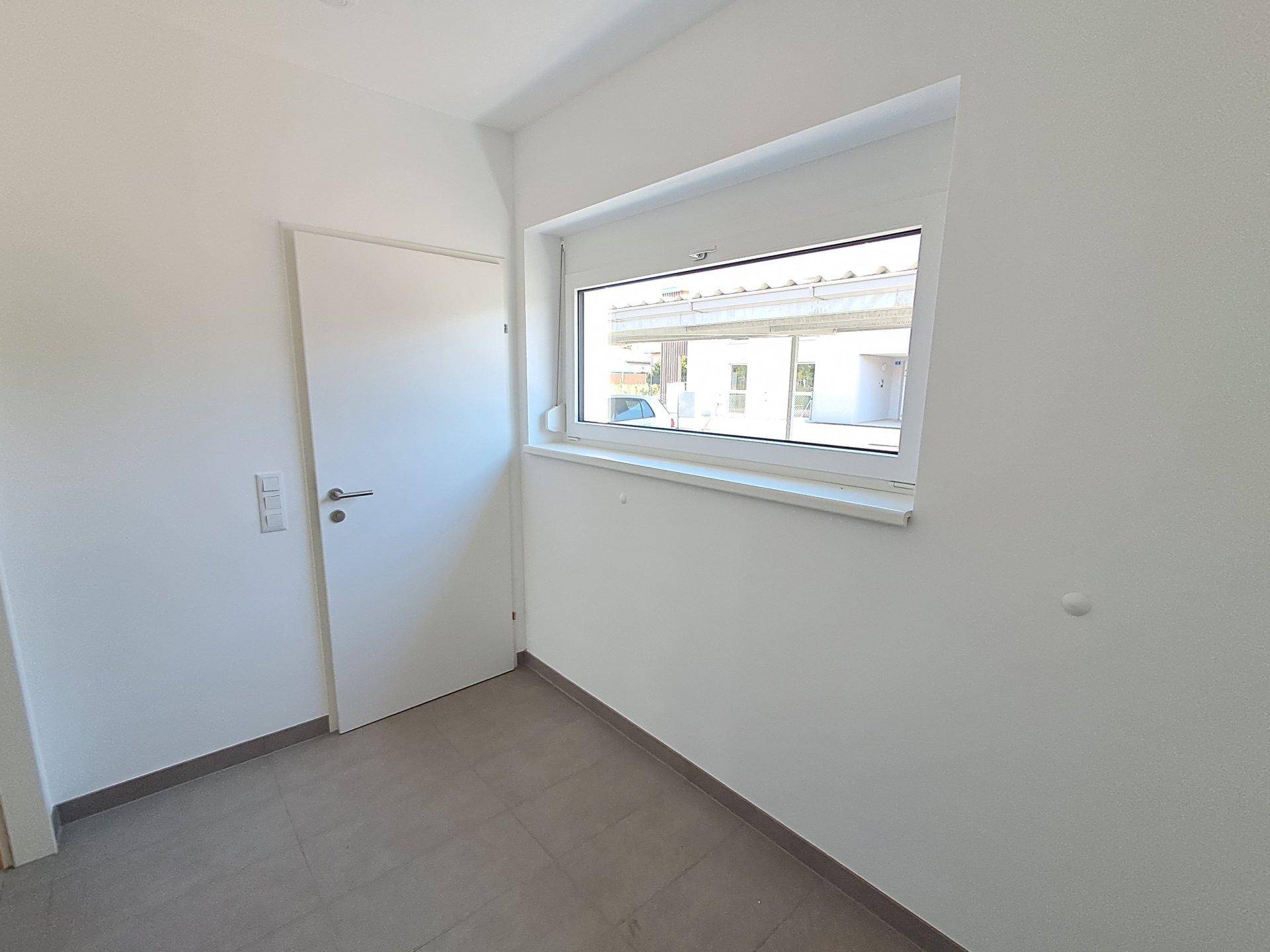 Heller Eingangsbereich mit Fliesenboden und Fenster, das Tageslicht hereinlässt.