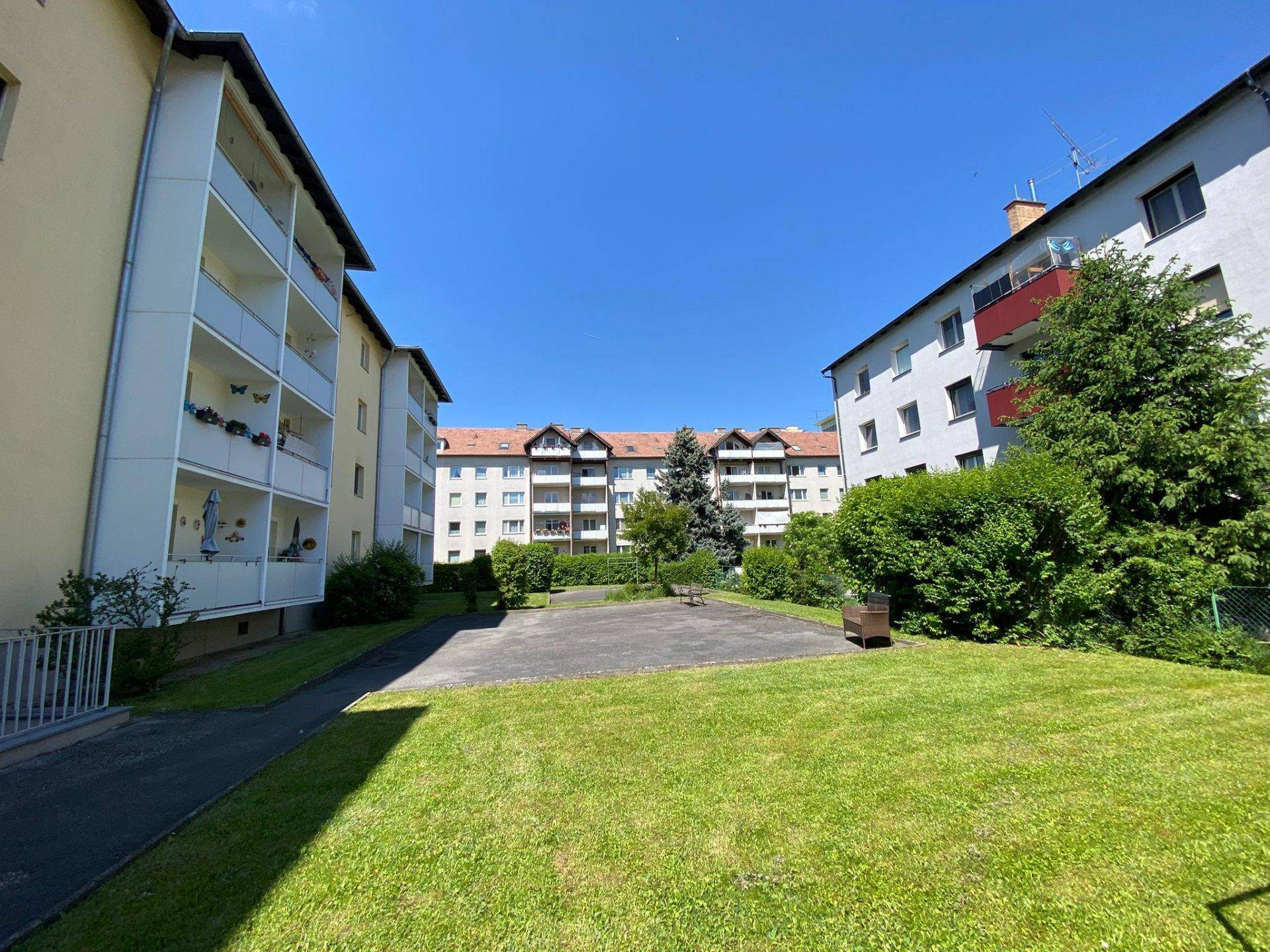 Innenhof mit Rasenfläche und umliegenden Wohngebäuden unter klarem blauem Himmel.