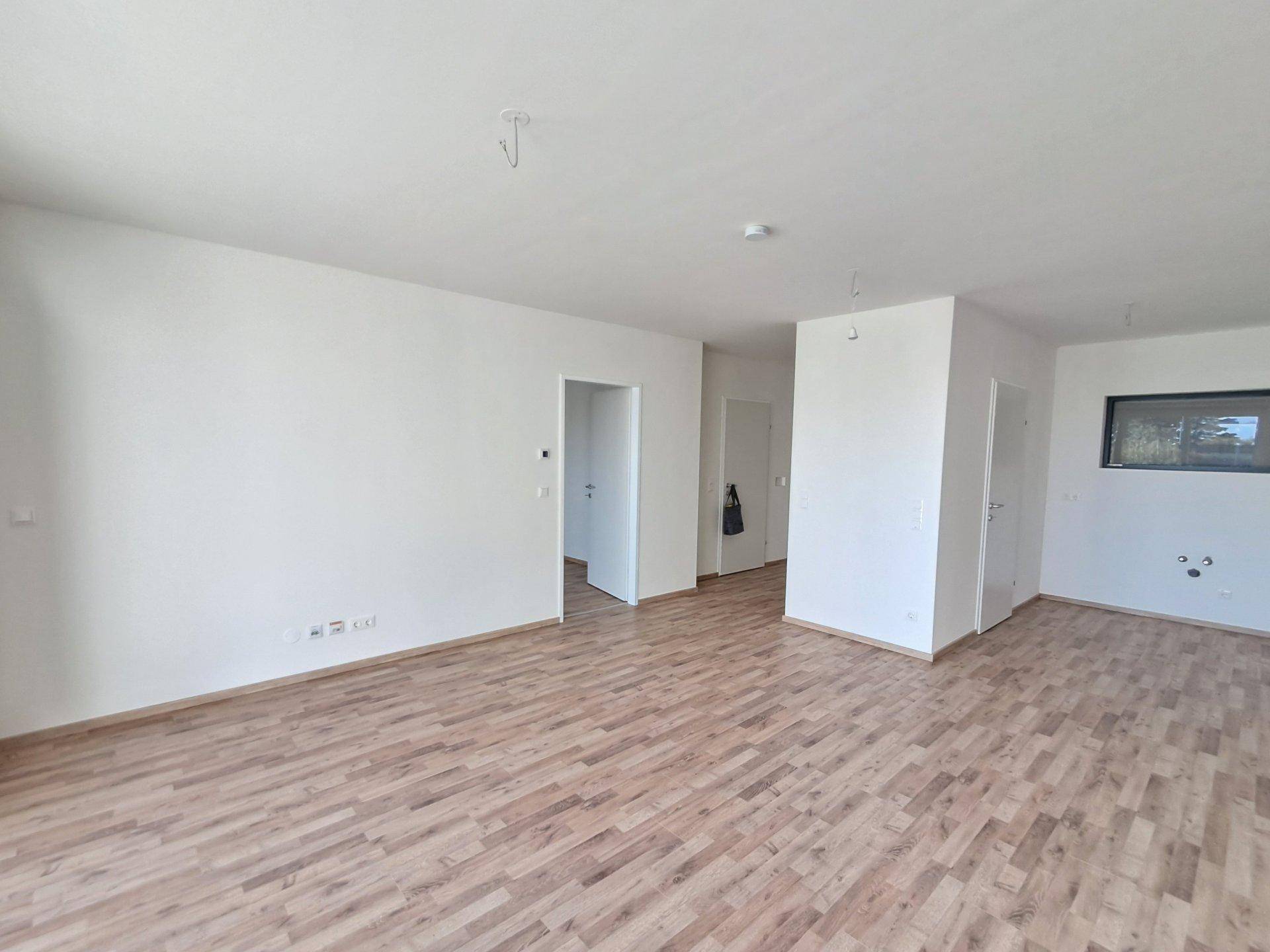 Geräumiger, unmöblierter Raum mit Holzboden und Zugang zu weiteren Zimmern.