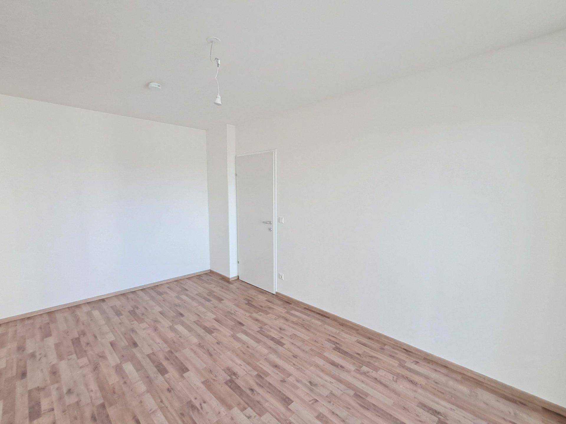 Leerer Raum mit Holzboden und weißen Wänden, vielseitig nutzbar.