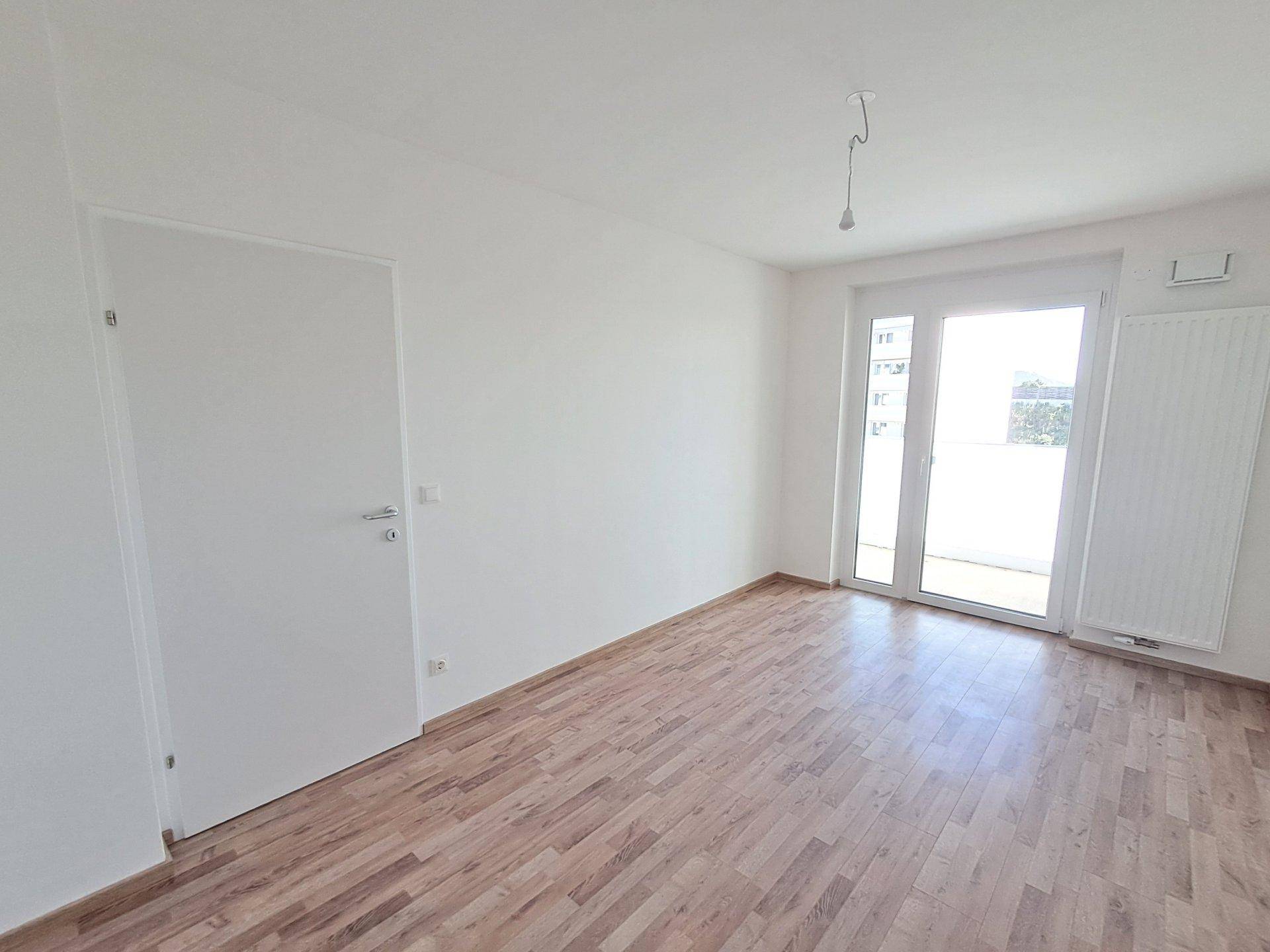 Heller, unmöblierter Raum mit Holzboden und Balkonzugang, ideal als Schlafzimmer.