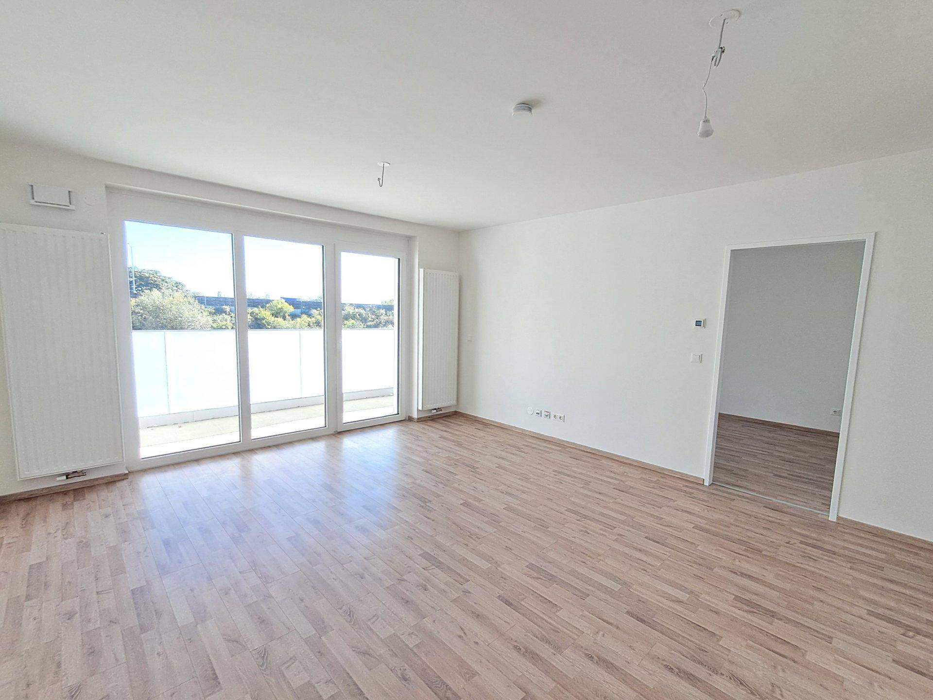 Heller, unmöblierter Raum mit großen Fenstern und direktem Zugang zum Balkon.
