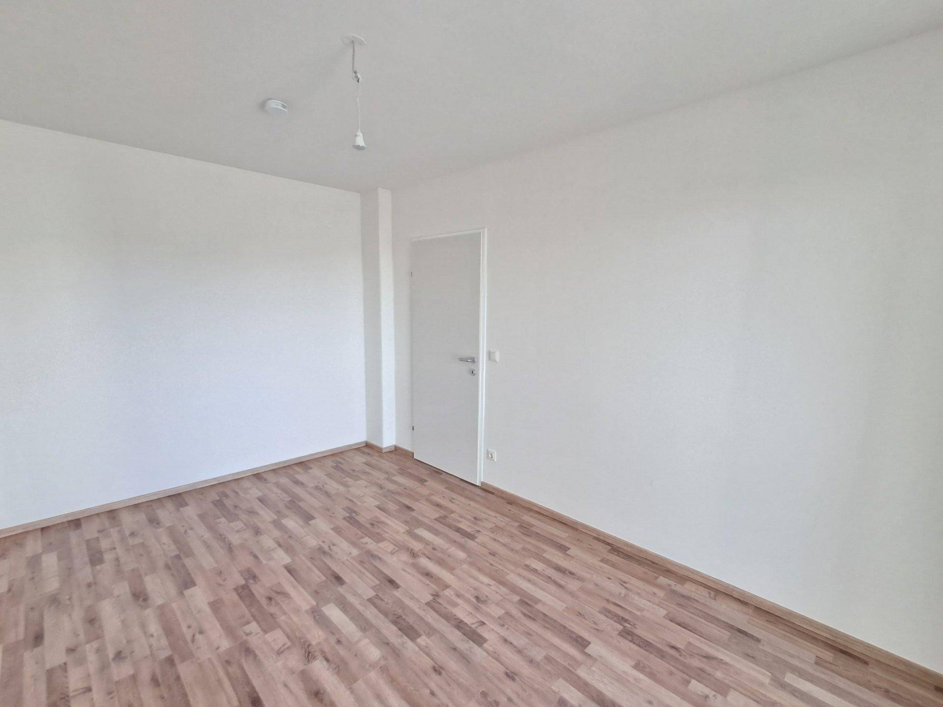 Leeres Schlafzimmer mit Holzboden und weißen Wänden, ideal für individuelle Gestaltung.
