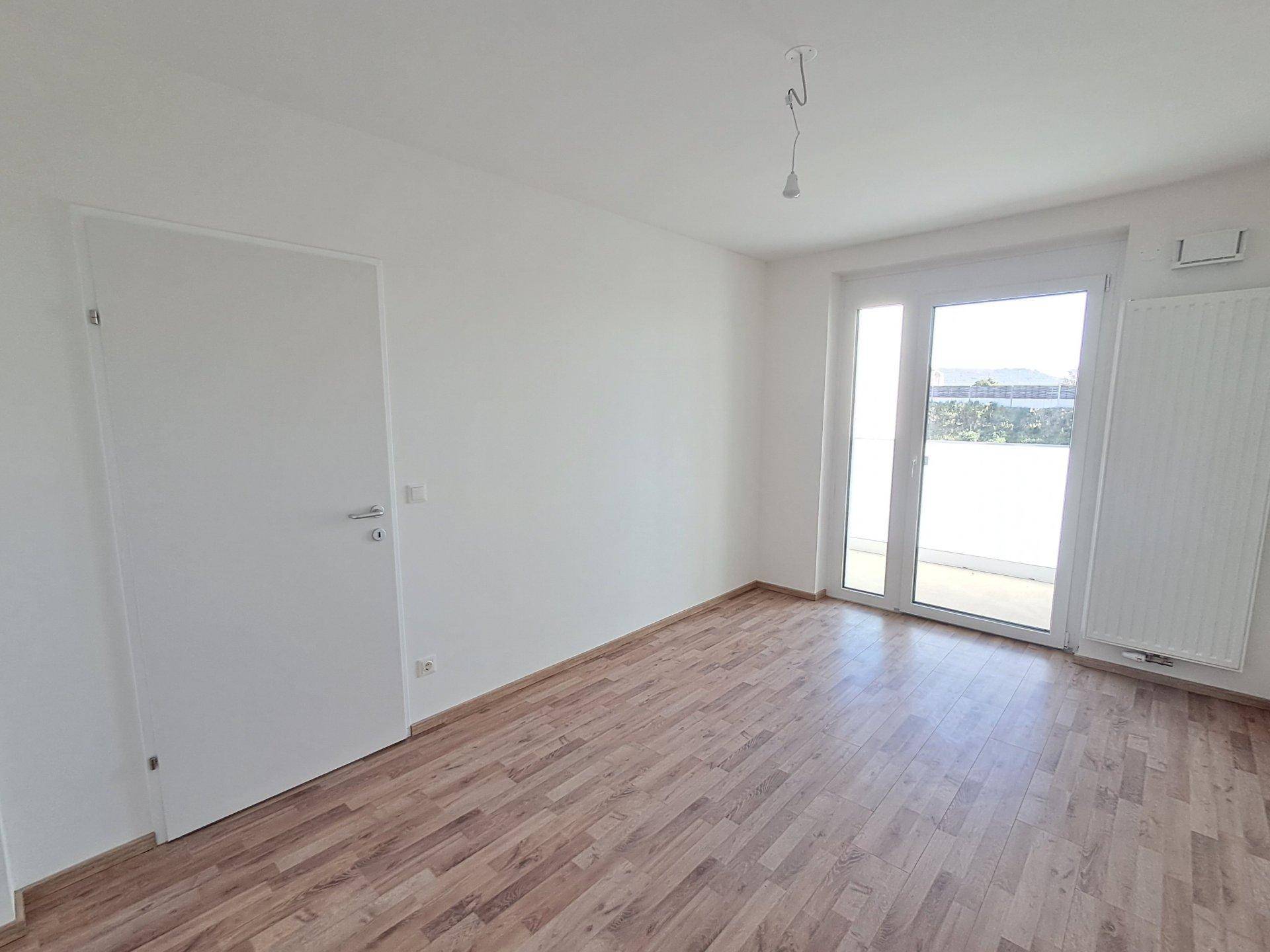 Helles, leeres Schlafzimmer mit Holzboden und großen Fenstern, bereit zur Einrichtung.