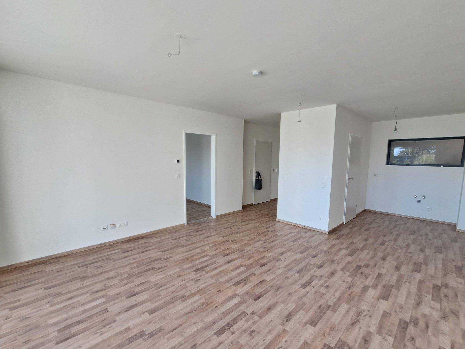 Heller Innenraum mit Holzboden und weißen Wänden, der verschiedene Bereiche verbindet.