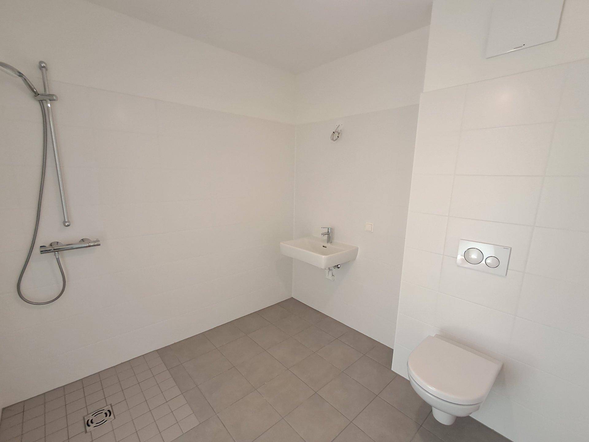 Helles, minimalistisches Badezimmer mit Dusche, Waschbecken und Wand-WC.