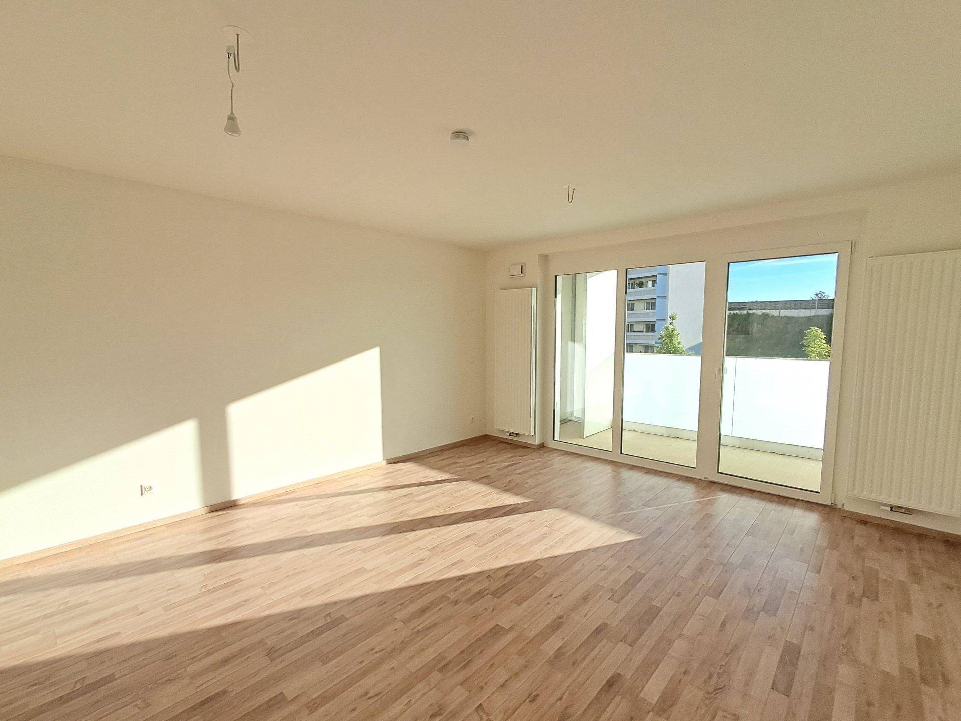 Heller, unmöblierter Raum mit großen Fenstern und Zugang zu einem Balkon.