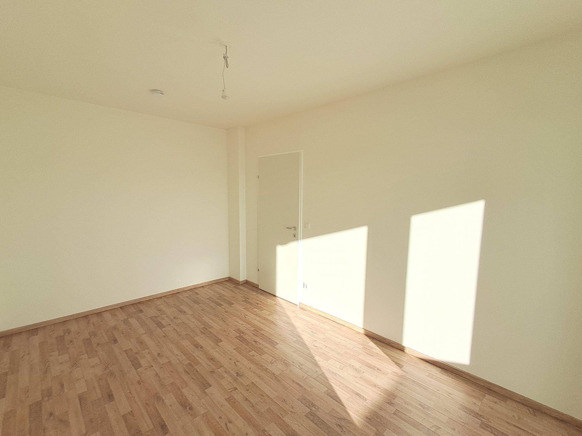 Leerer Raum mit hellem Holzfußboden und weiß gestrichenen Wänden, gut beleuchtet.