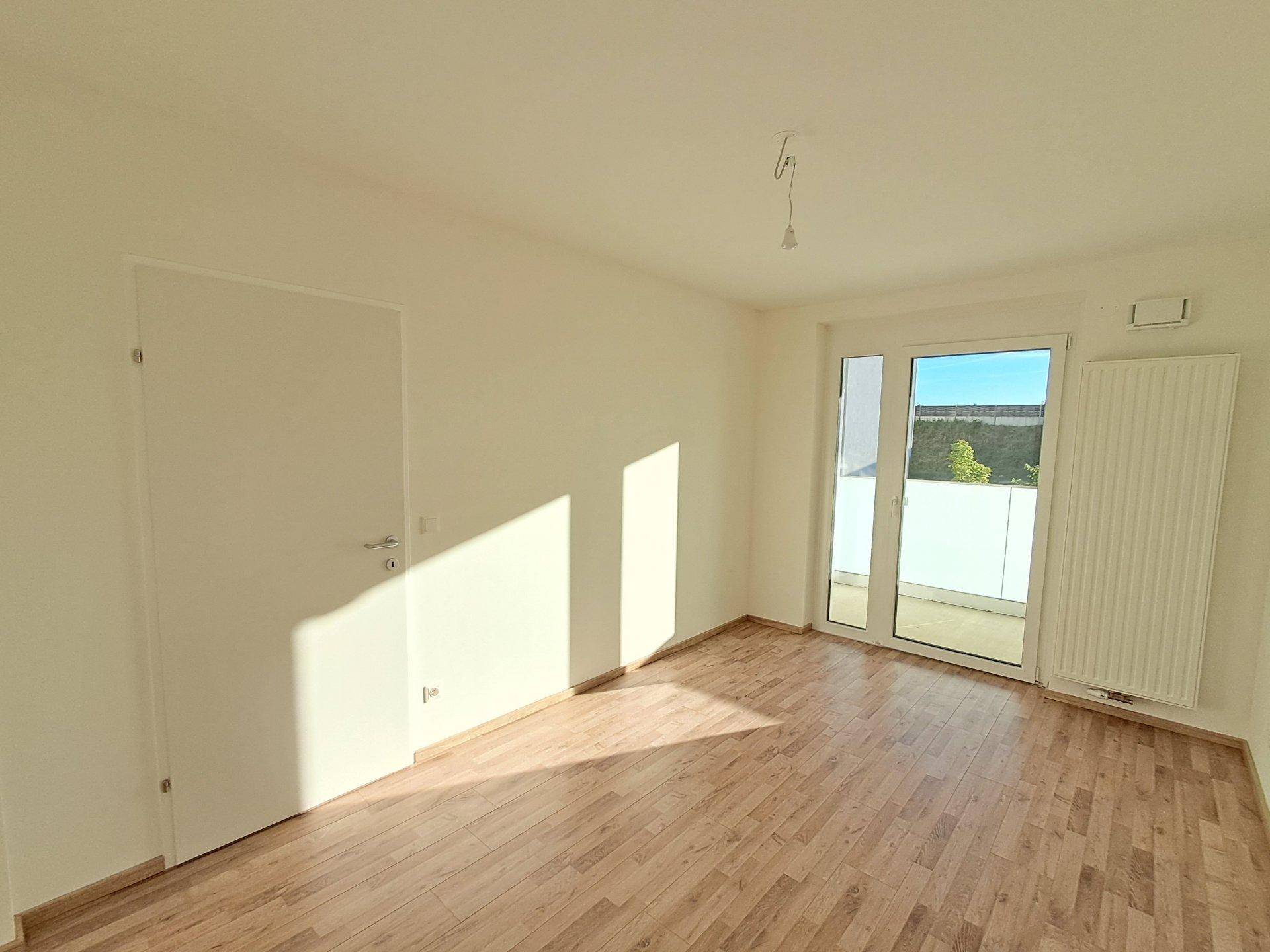 Unmöblierter Raum mit großen Fenstern, die viel Sonnenlicht hereinlassen.