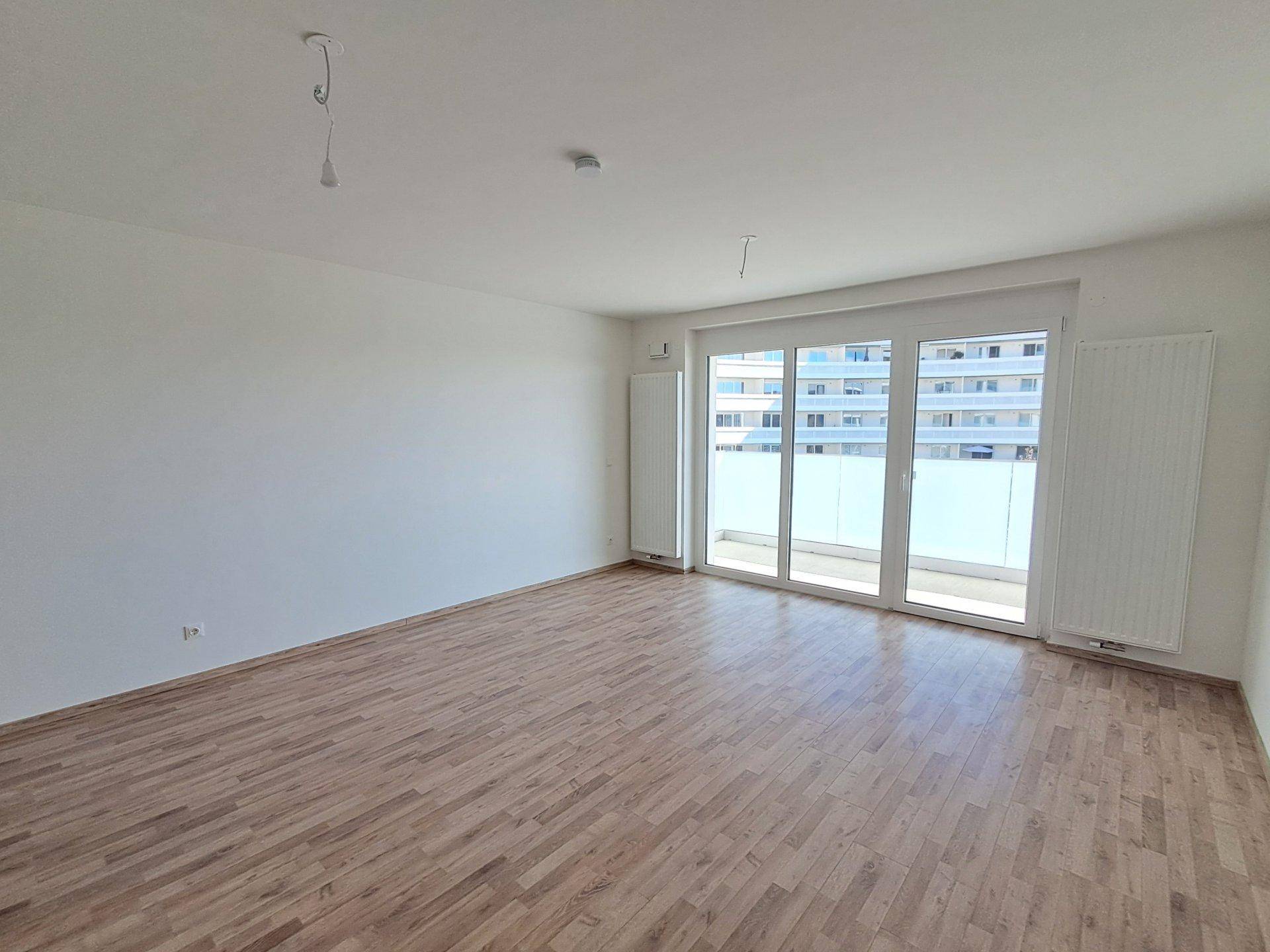 Geräumiger, unmöblierter Raum mit Holzboden und breiter Fensterfront, die den Blick auf die Umgebung freigibt.