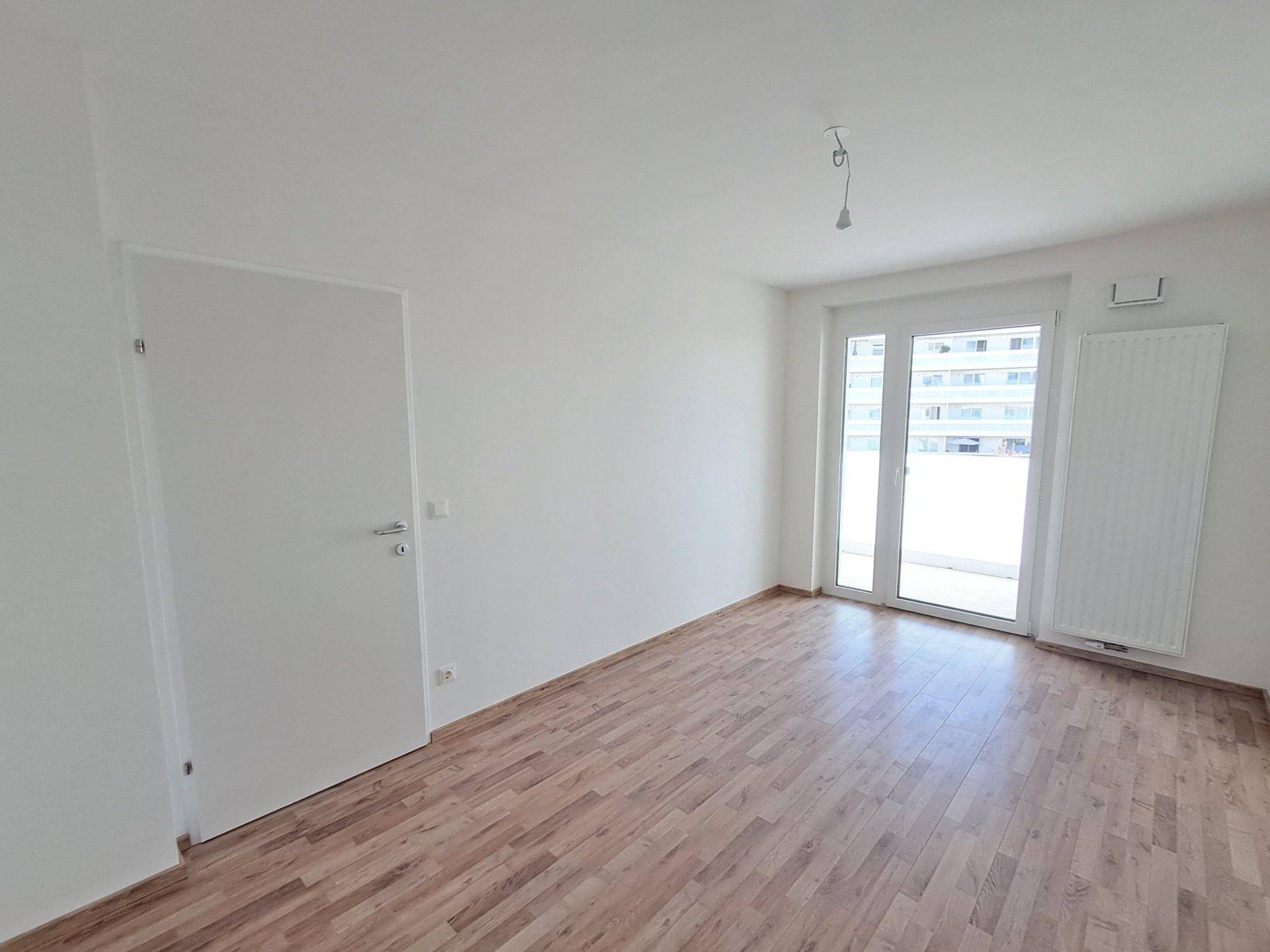 Geräumiger, unmöblierter Raum mit Holzboden und einer breiten Fensterfront, die den Raum erhellt.