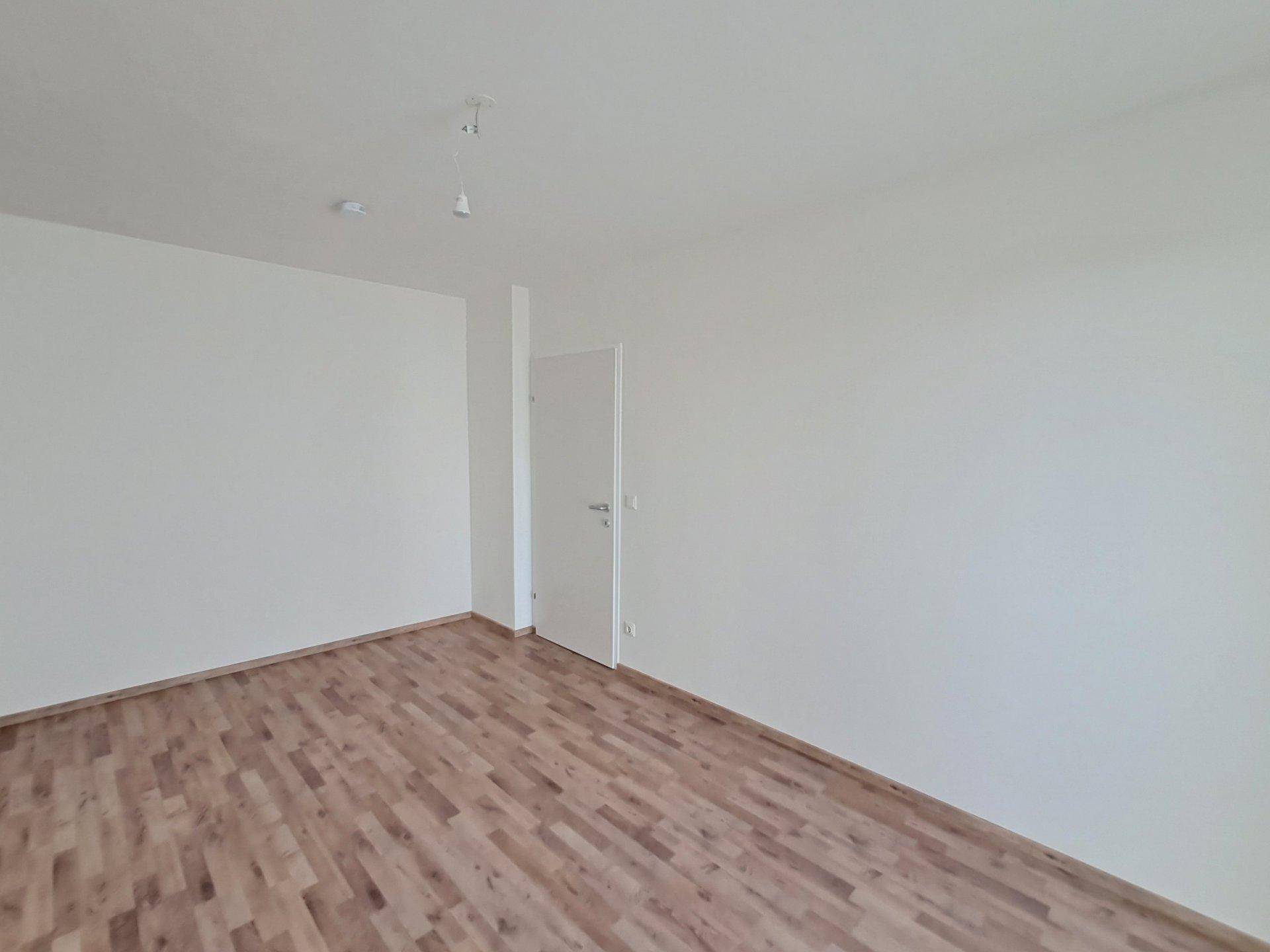 Heller, leerer Raum mit Holzboden und einer Tür, der vielseitig genutzt werden kann.