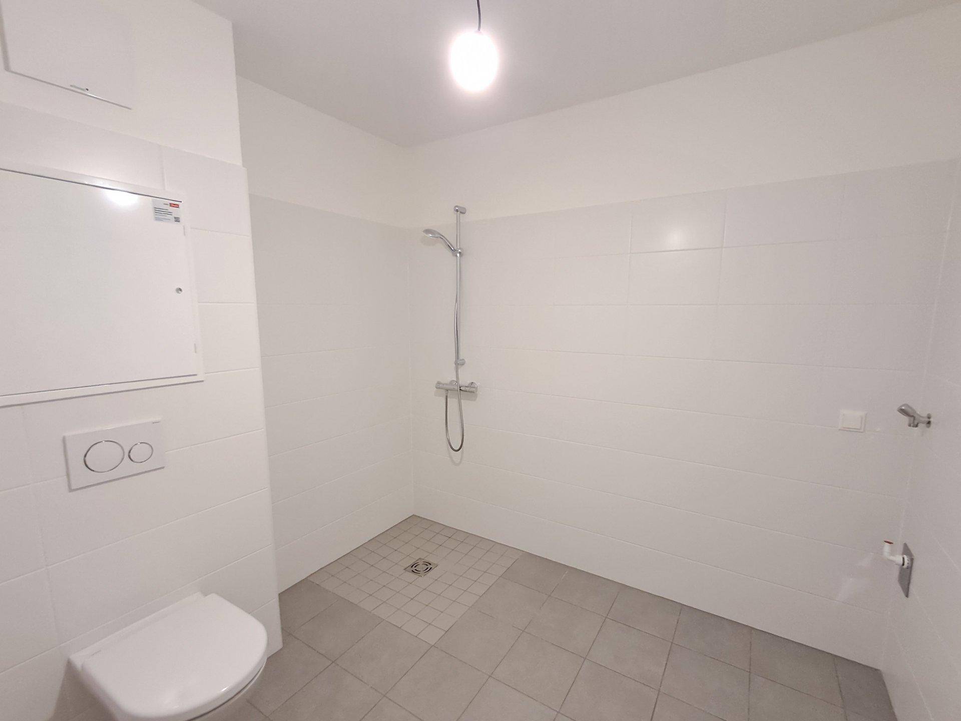 Helles Badezimmer mit Duschbereich und Wand-WC, ausgestattet mit modernen Fliesen.