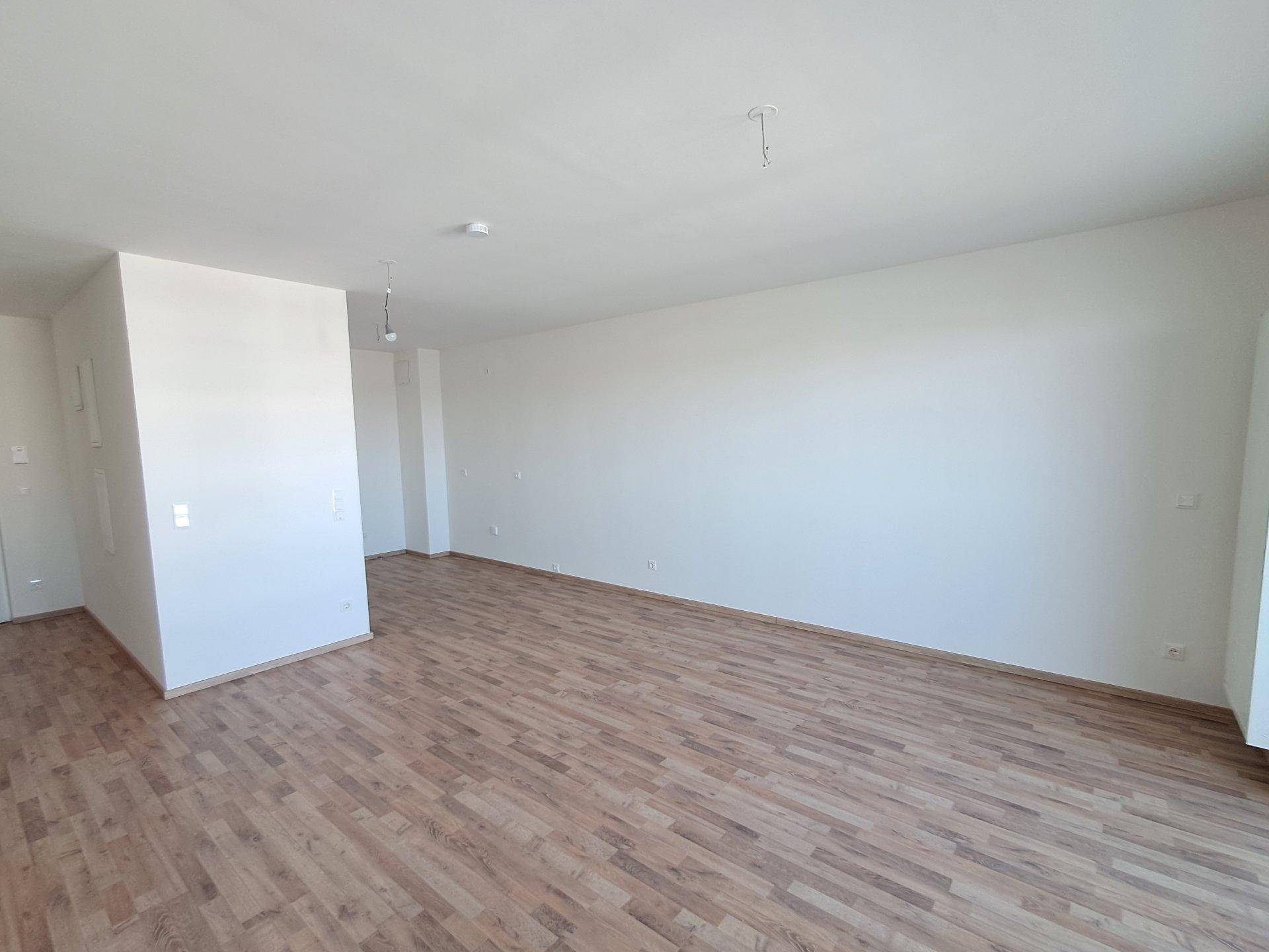 Geräumiger, unmöblierter Wohnbereich mit hellem Holzfußboden und viel Tageslicht.