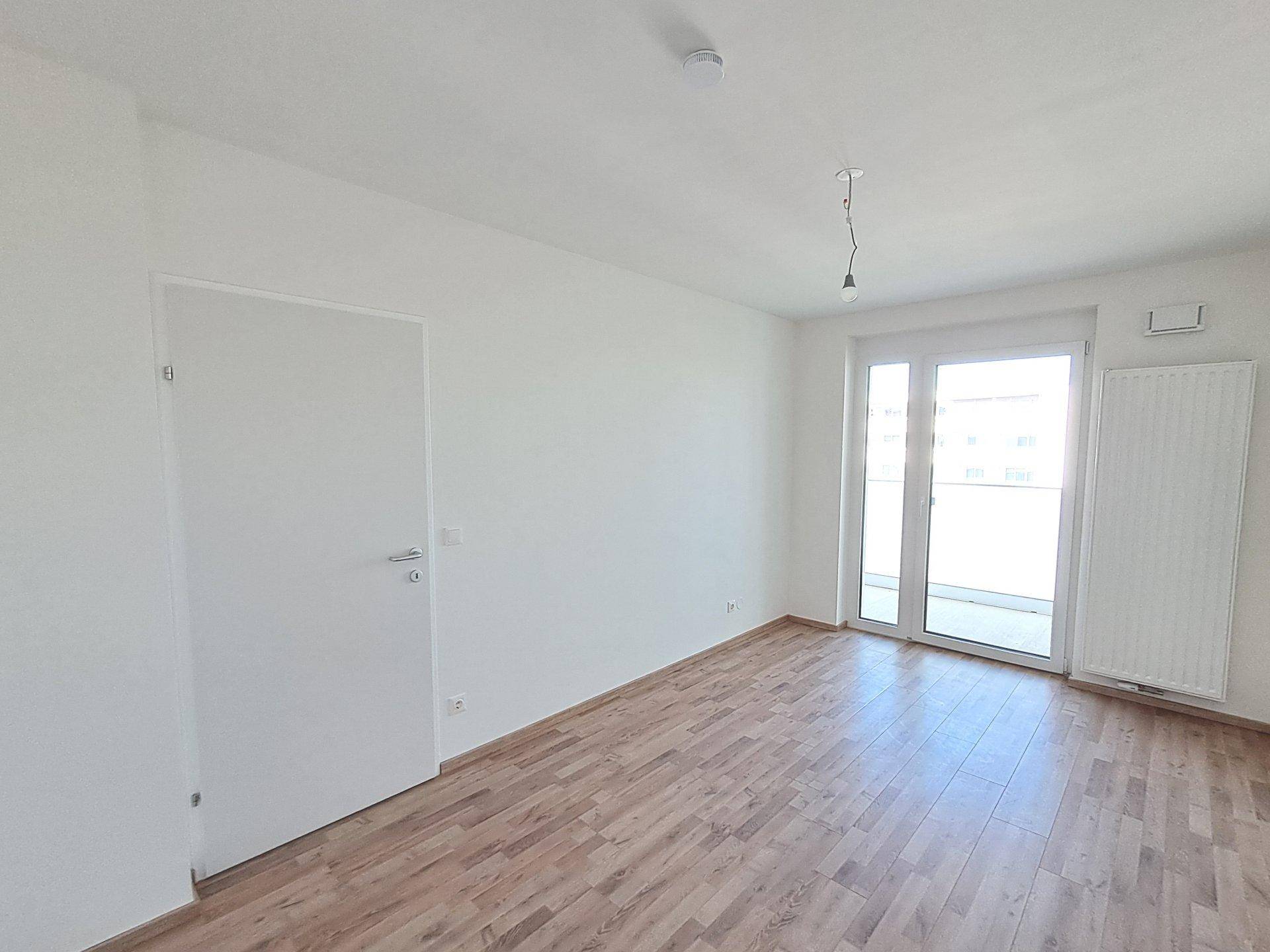 Helles, unmöbliertes Schlafzimmer mit Holzfußboden und Zugang zu einem Balkon.