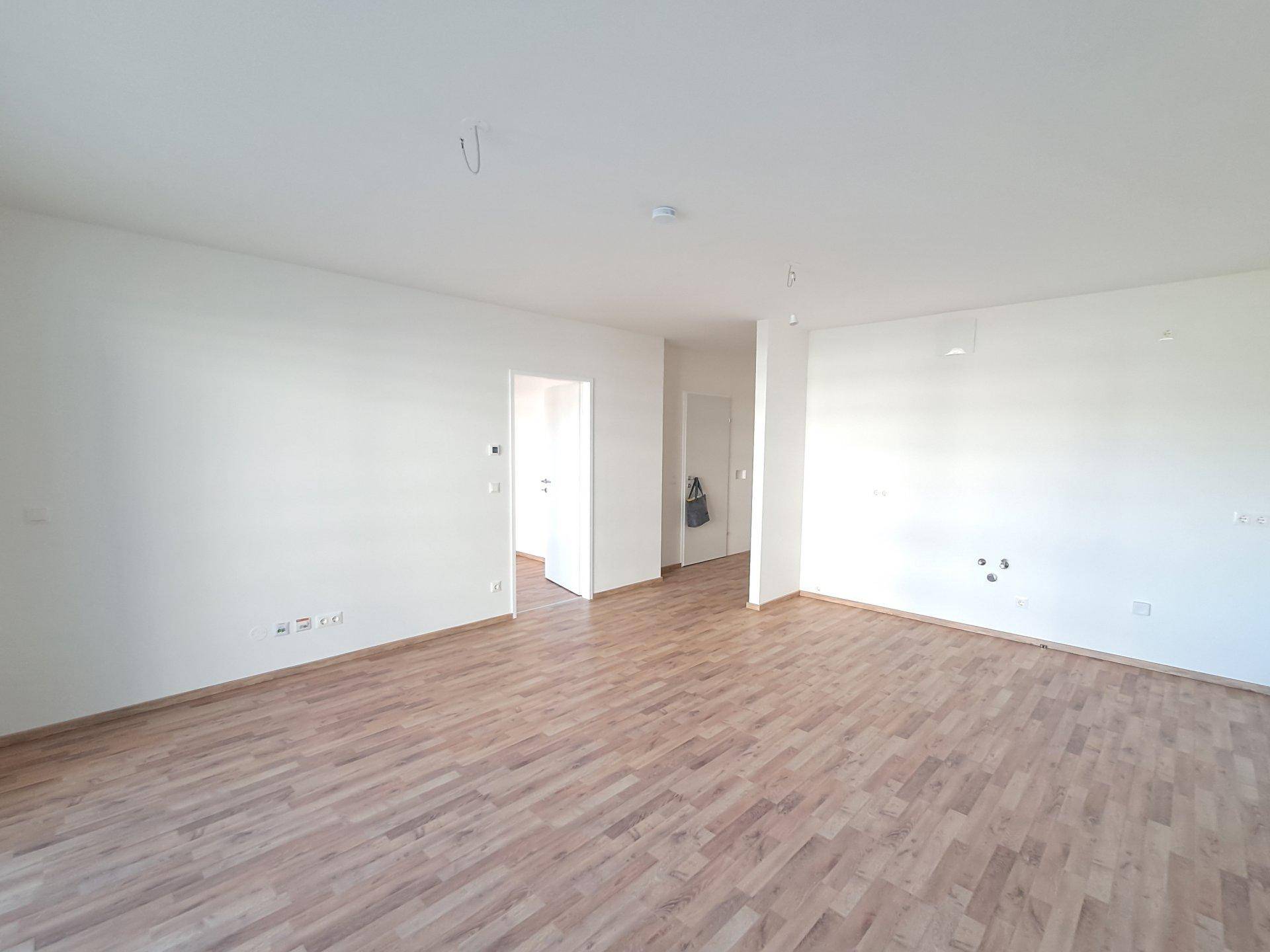 Heller, leerer Wohnbereich mit Laminatboden und weißen Wänden, bereit zur individuellen Einrichtung.