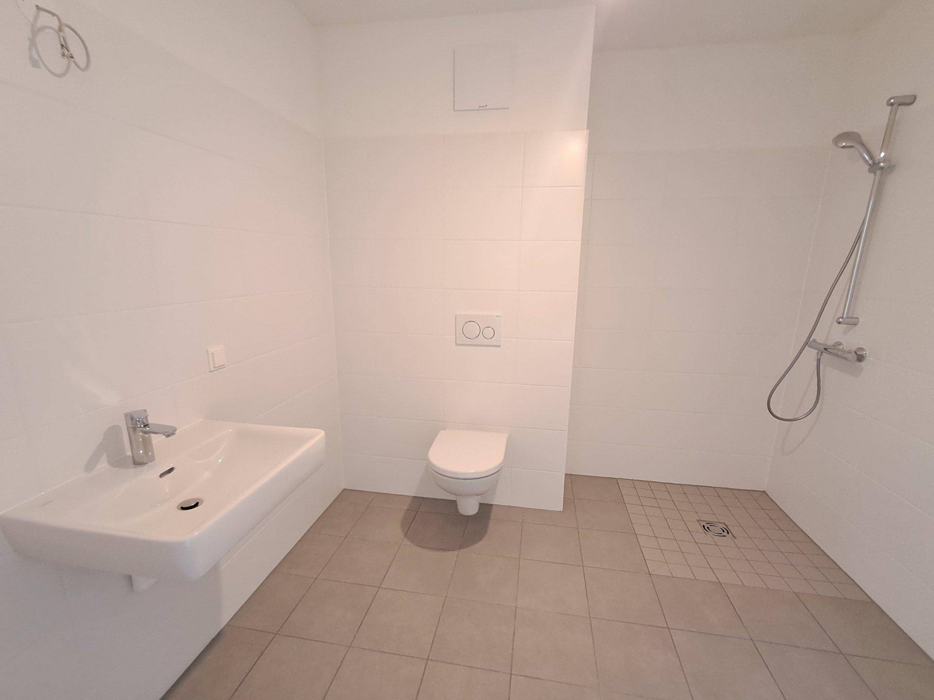 Unmöbliertes Badezimmer mit Dusche, WC und Waschbecken, bereit zur individuellen Gestaltung.