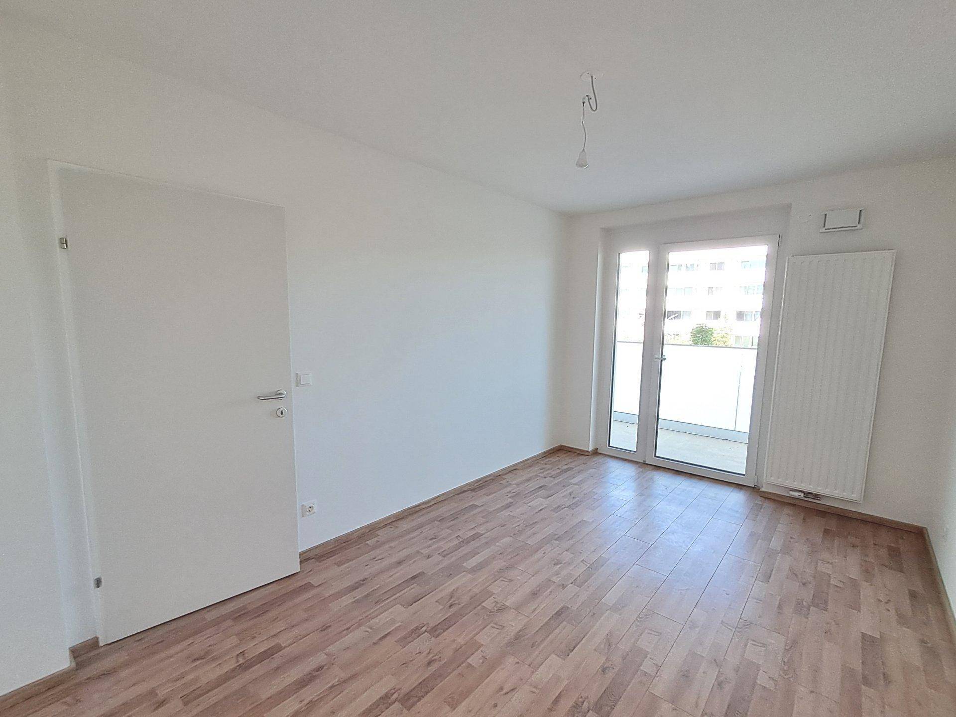 Helles, unmöbliertes Schlafzimmer mit Laminatboden und Zugang zu einem sonnigen Balkon.