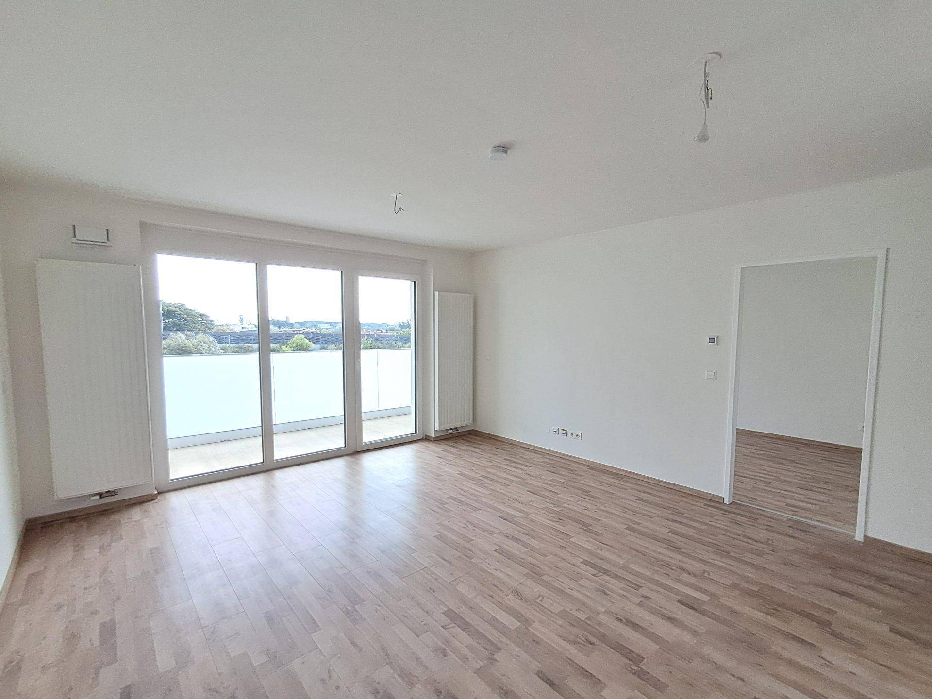 Geräumiger, unmöblierter Wohnbereich mit großen Fenstern und direktem Balkonzugang.
