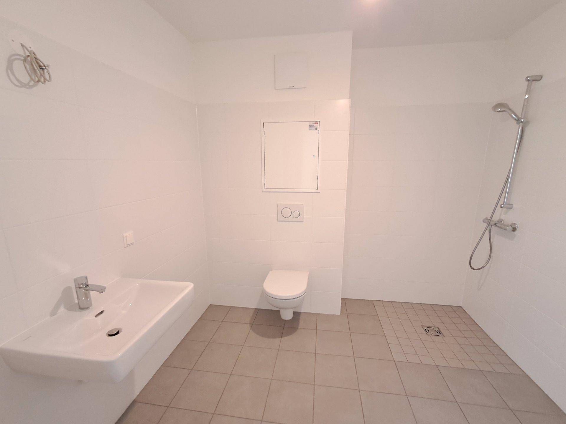 Unmöbliertes Badezimmer mit Fliesenboden, Wand-WC und Duschbereich, bereit zur Gestaltung.