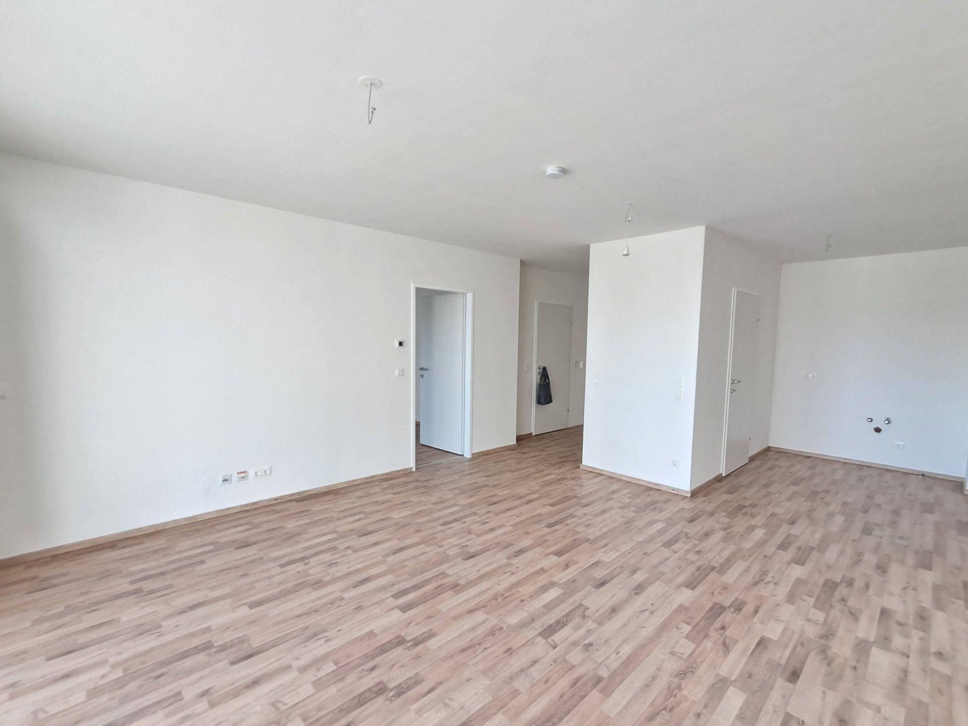 Heller, leerer Wohnbereich mit Holzboden und weißen Wänden, bereit zur individuellen Gestaltung.