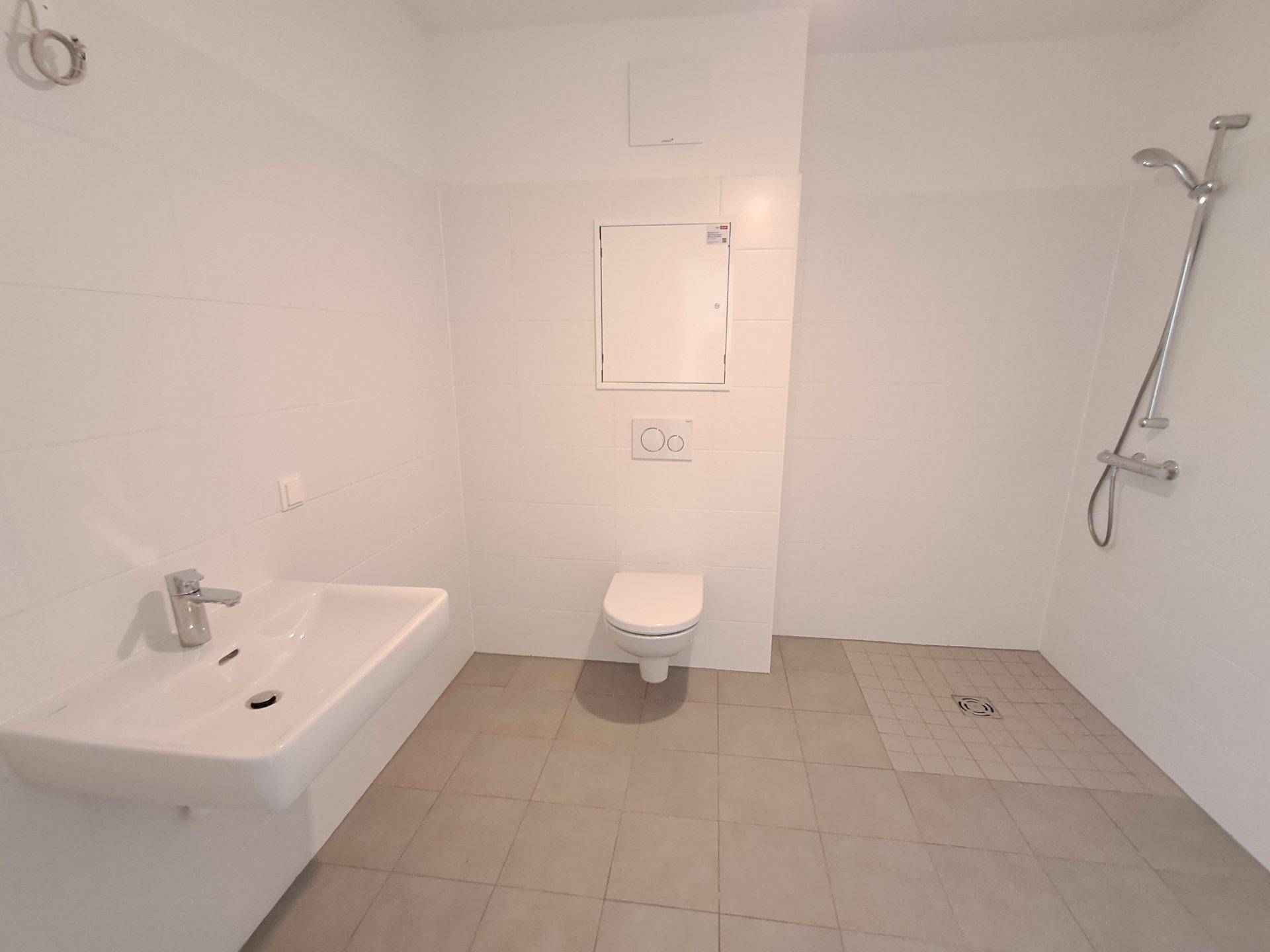 Helles Badezimmer mit weiß gefliesten Wänden, ebenerdiger Dusche und modernem Waschbecken.