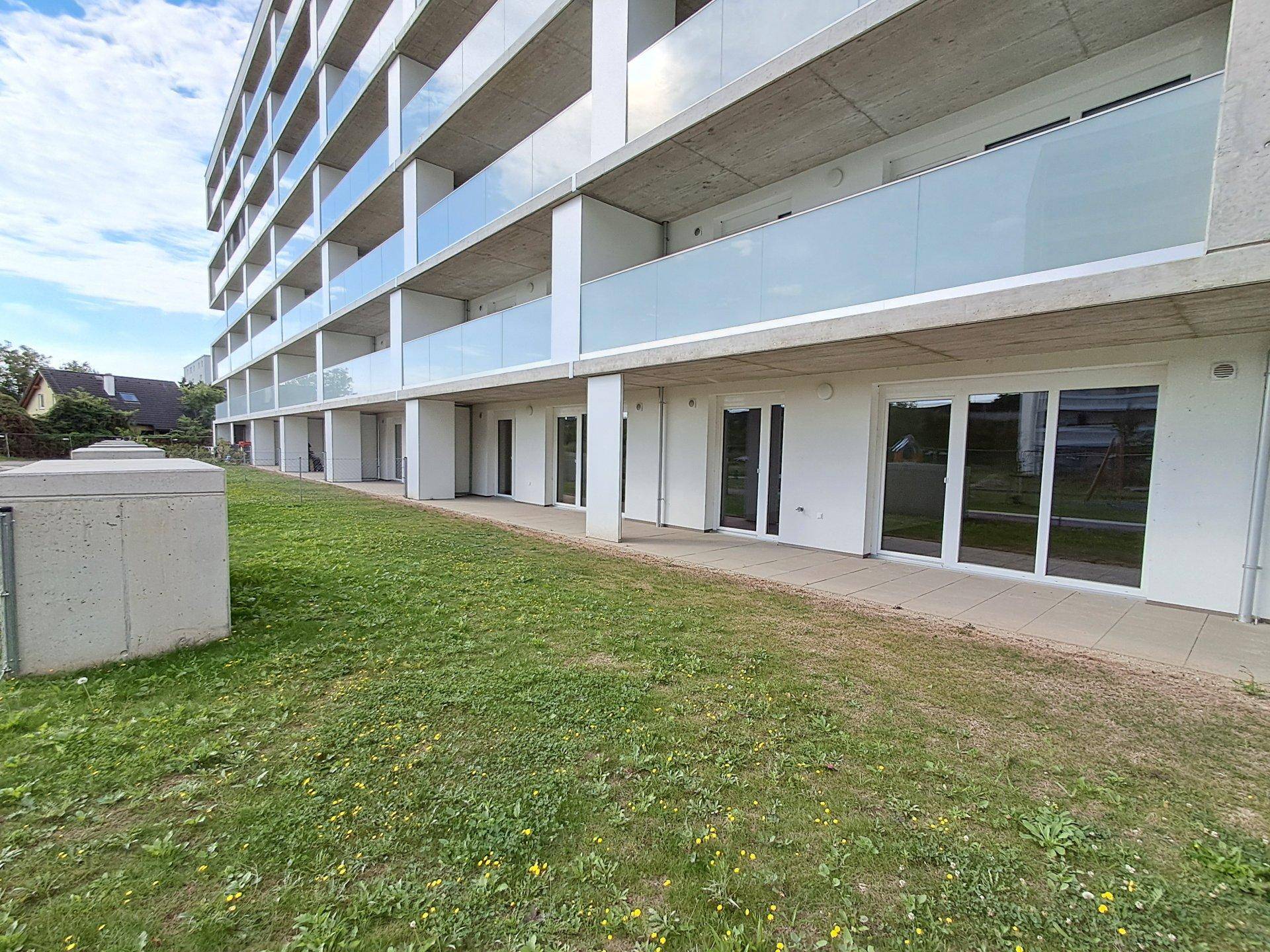 Moderne Wohnanlage mit Terrassen im Erdgeschoss und gepflegter Rasenfläche, umgeben von Grün.