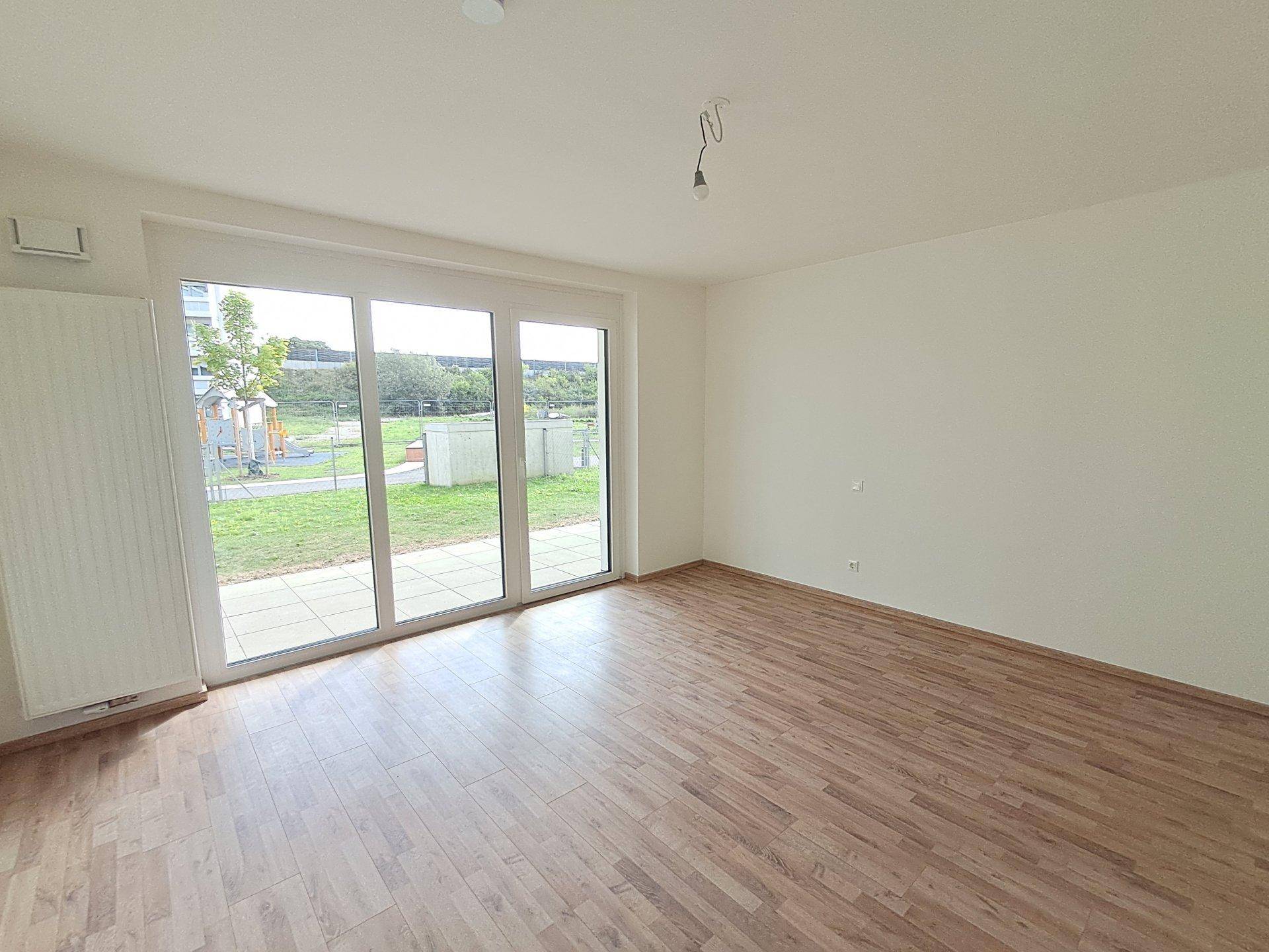 Geräumiges Zimmer mit Laminatboden und großen Schiebetüren, die zu einer Terrasse und Rasenfläche führen.