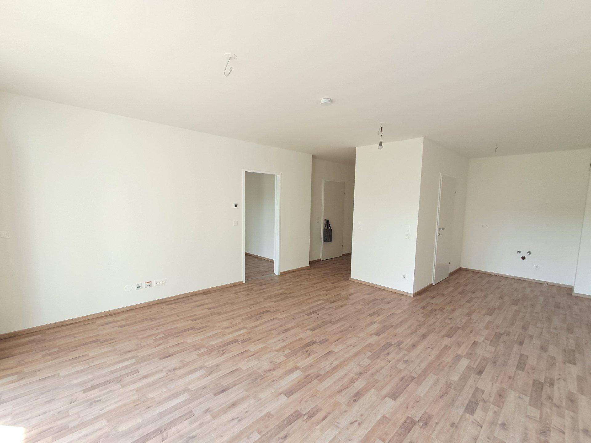 Leerer Raum mit Holzoptikboden und weißen Wänden, bereit zur individuellen Gestaltung.