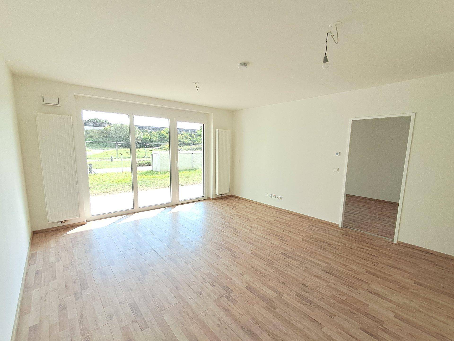 Heller, leerer Raum mit Holzoptikboden und großen Schiebetüren zum sonnigen Außenbereich.