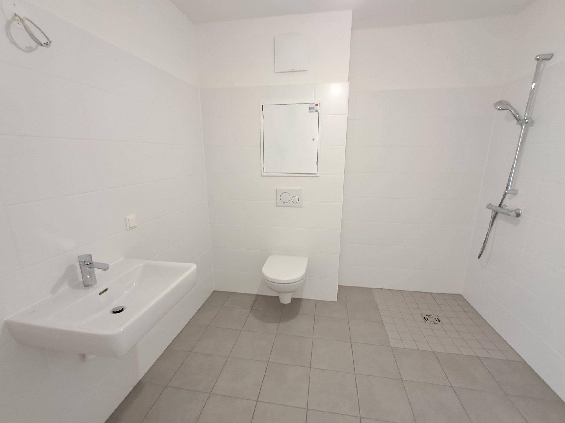 Unmöbliertes Badezimmer mit Duschbereich, Wand-WC und Waschbecken, hell gefliest und funktional.