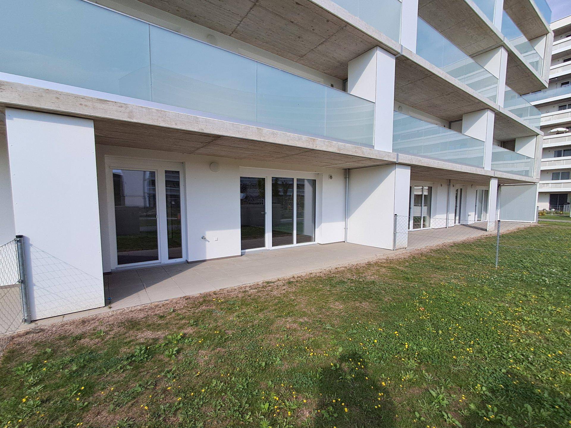 Erdgeschossfassade eines modernen Gebäudes mit Terrassenzugängen und gepflegten Grünflächen.