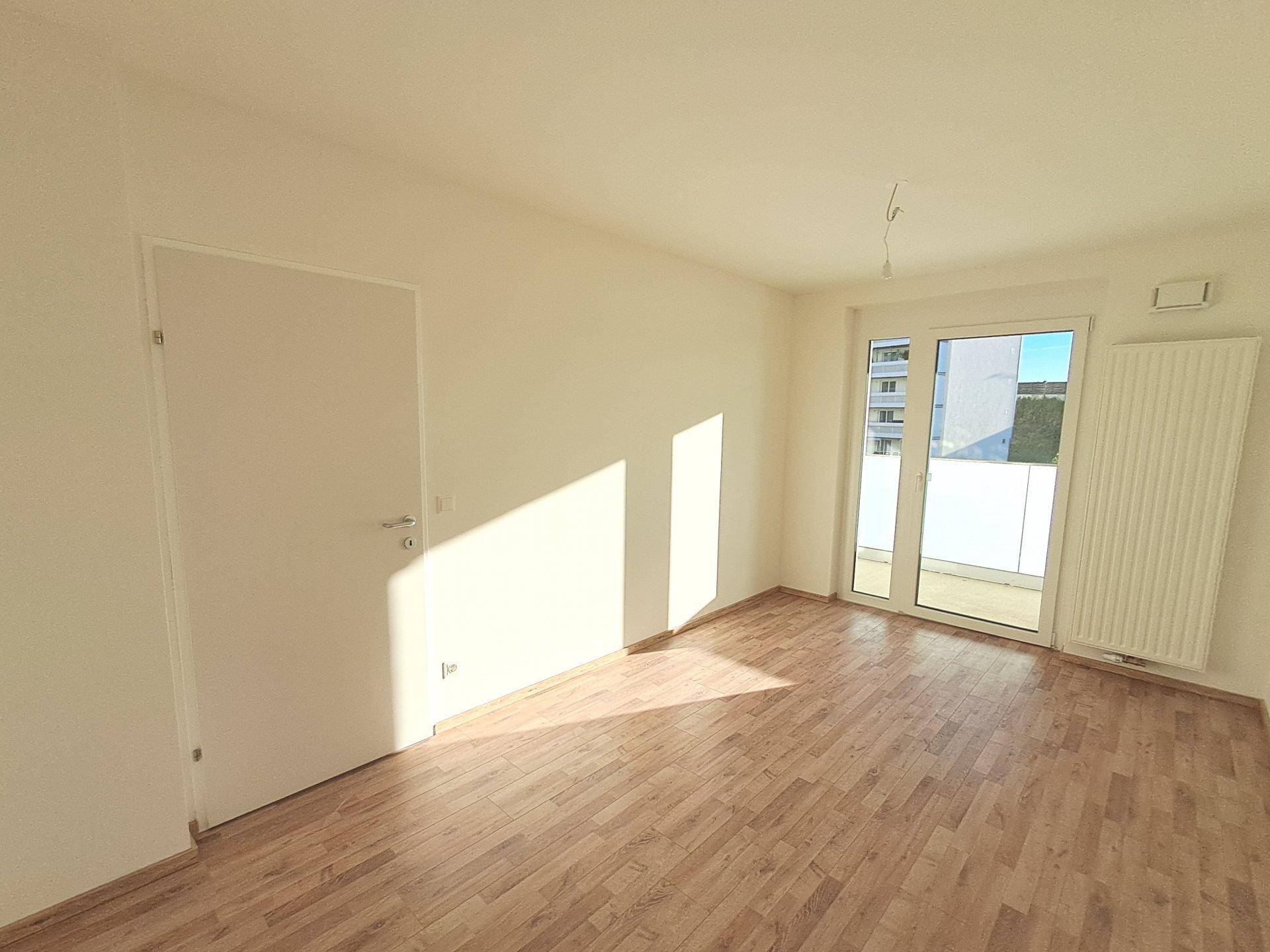 Leeres, helles Zimmer mit Laminatboden und großen Fenstern, die Zugang zu einem Balkon bieten und viel Licht hereinlassen.