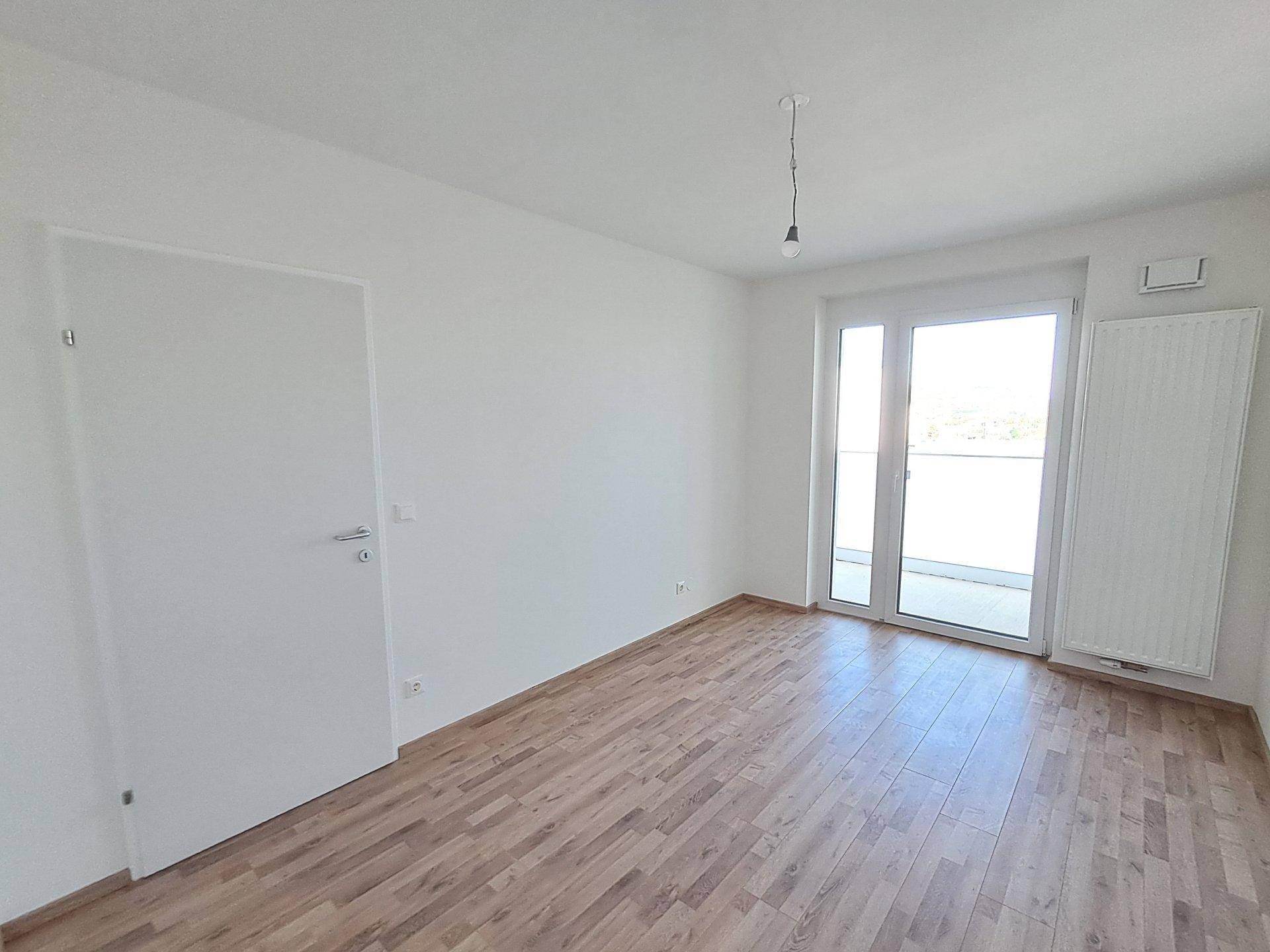 Leeres Schlafzimmer mit Holzfußboden und großem Fenster zum Außenbereich.
