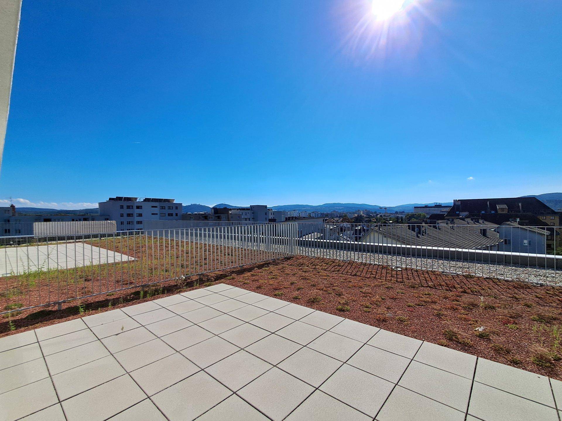 Sonnige Dachterrasse mit Fliesen und weitem Blick über die Stadt und die Berge.