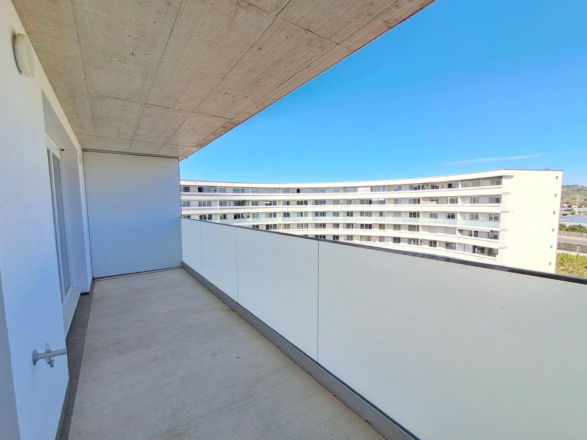 Heller Balkon mit moderner Glasbrüstung und Blick auf umliegende Gebäude.