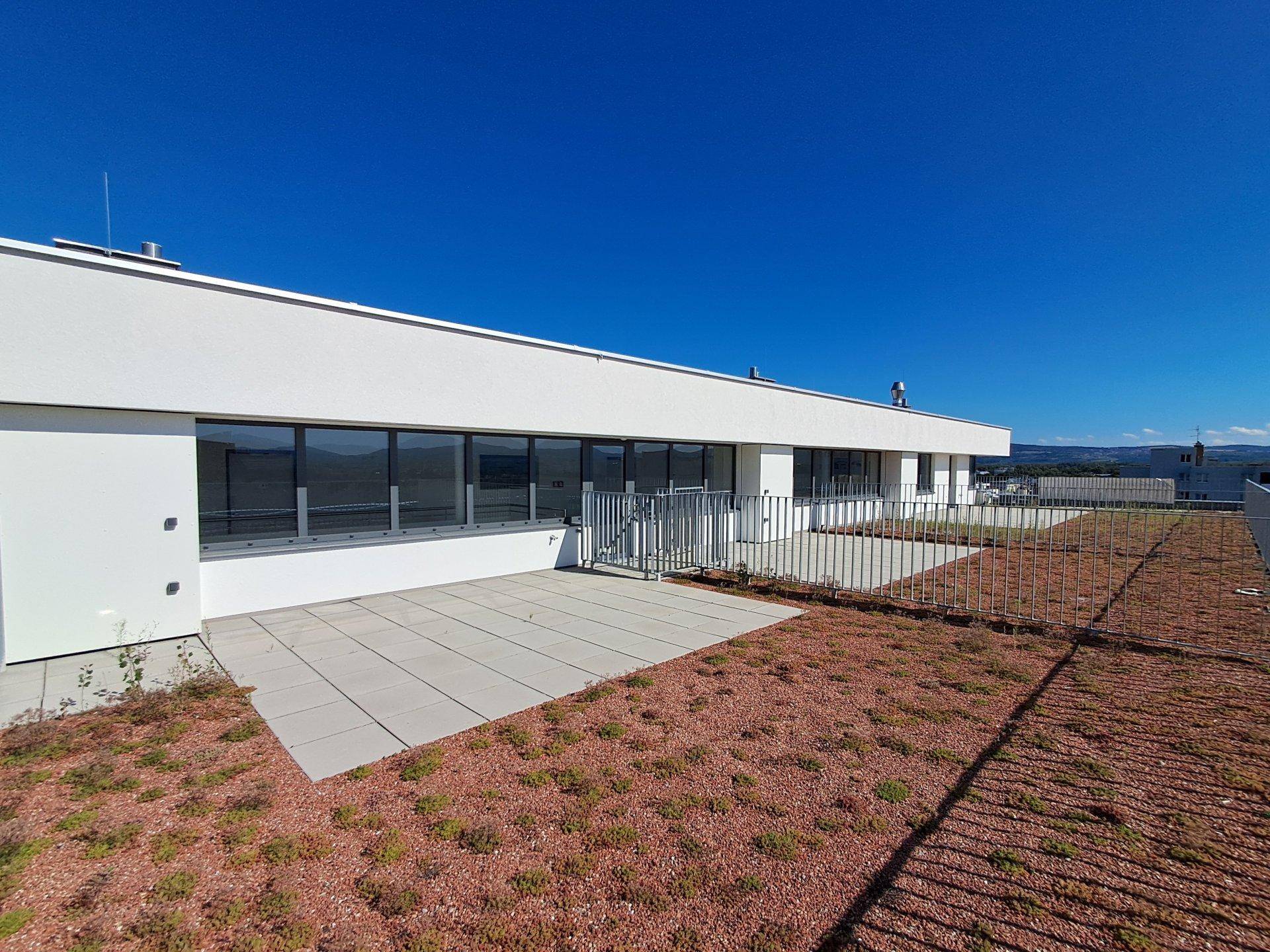 Weitläufige Dachterrasse mit Fliesen und Grünflächen, bietet viel Platz im Freien.